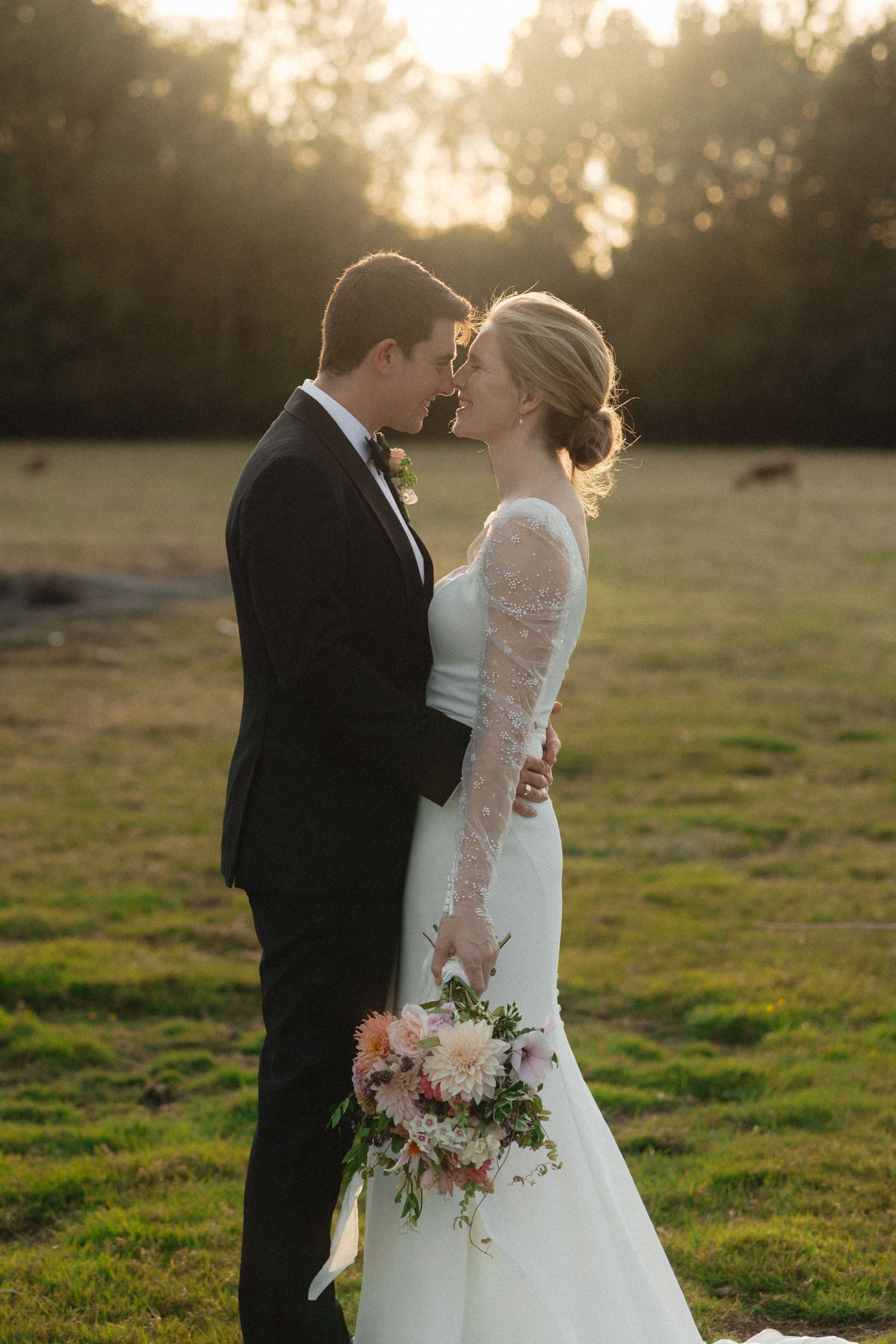 Golden hour wedding portrait with couple embracing in sunlit field.