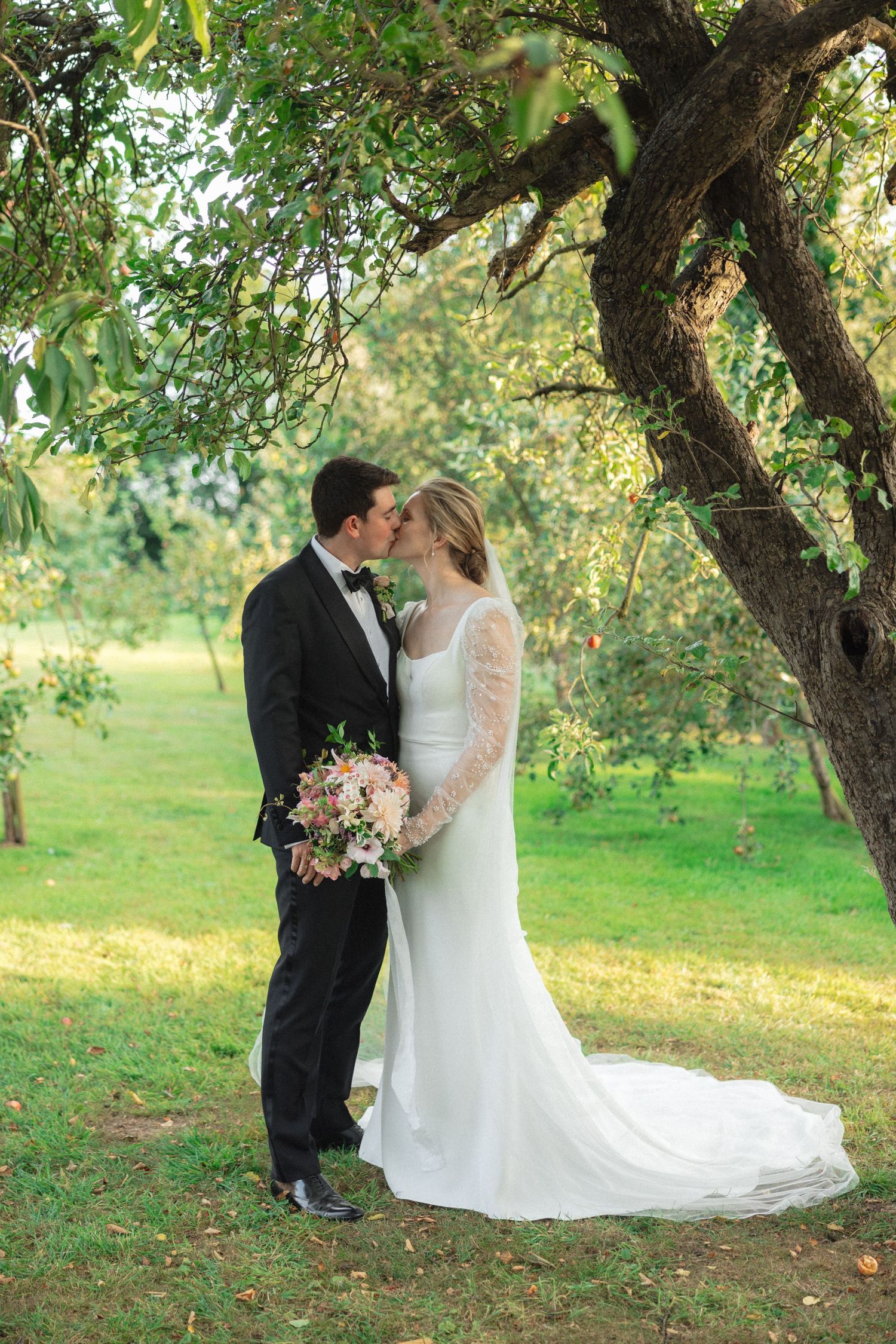 Romantic wedding couple poses under blooming apple trees in an orchard.