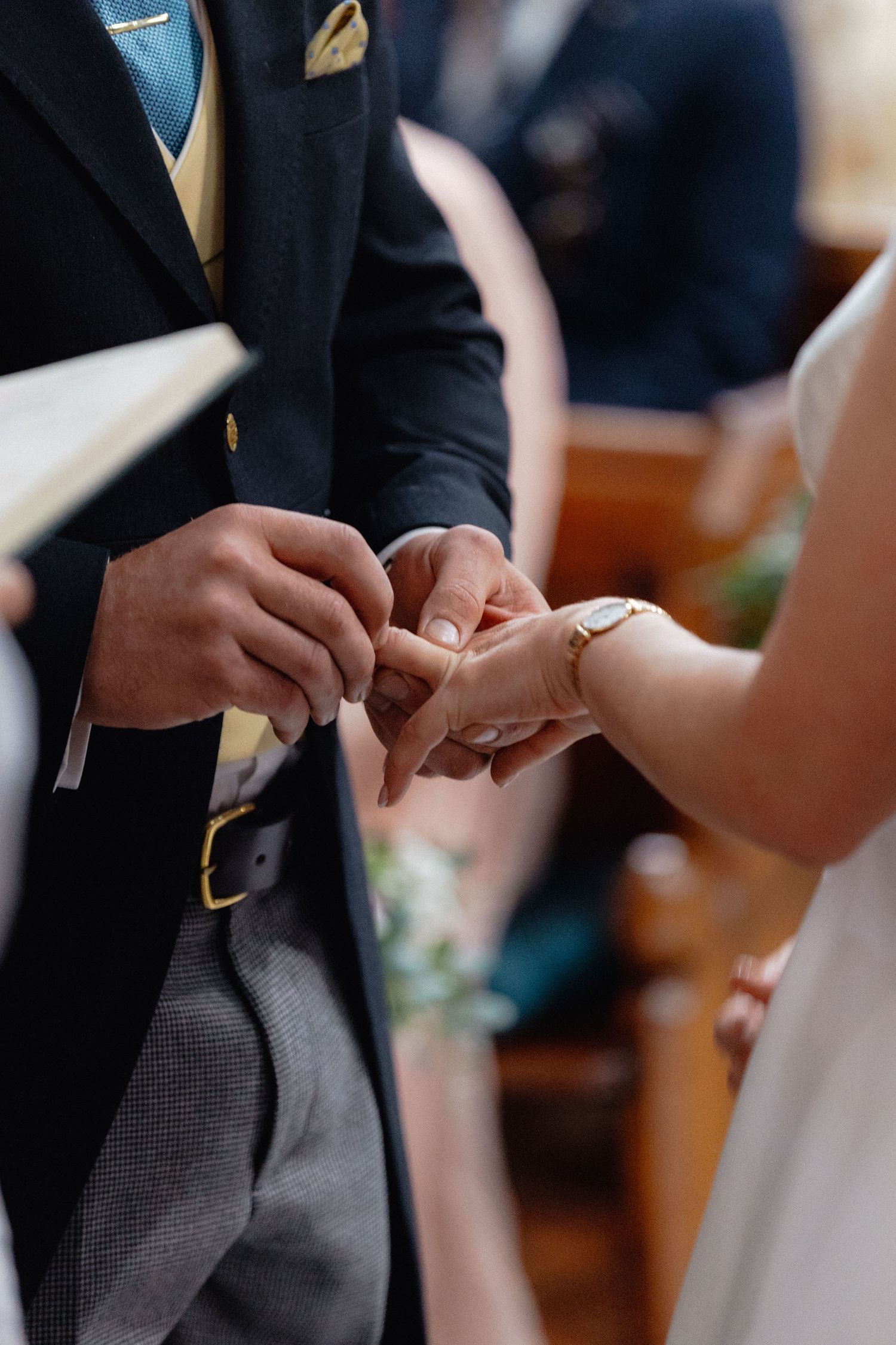 Close-up of wedding ring exchange during ceremony showing hands and formal attire.