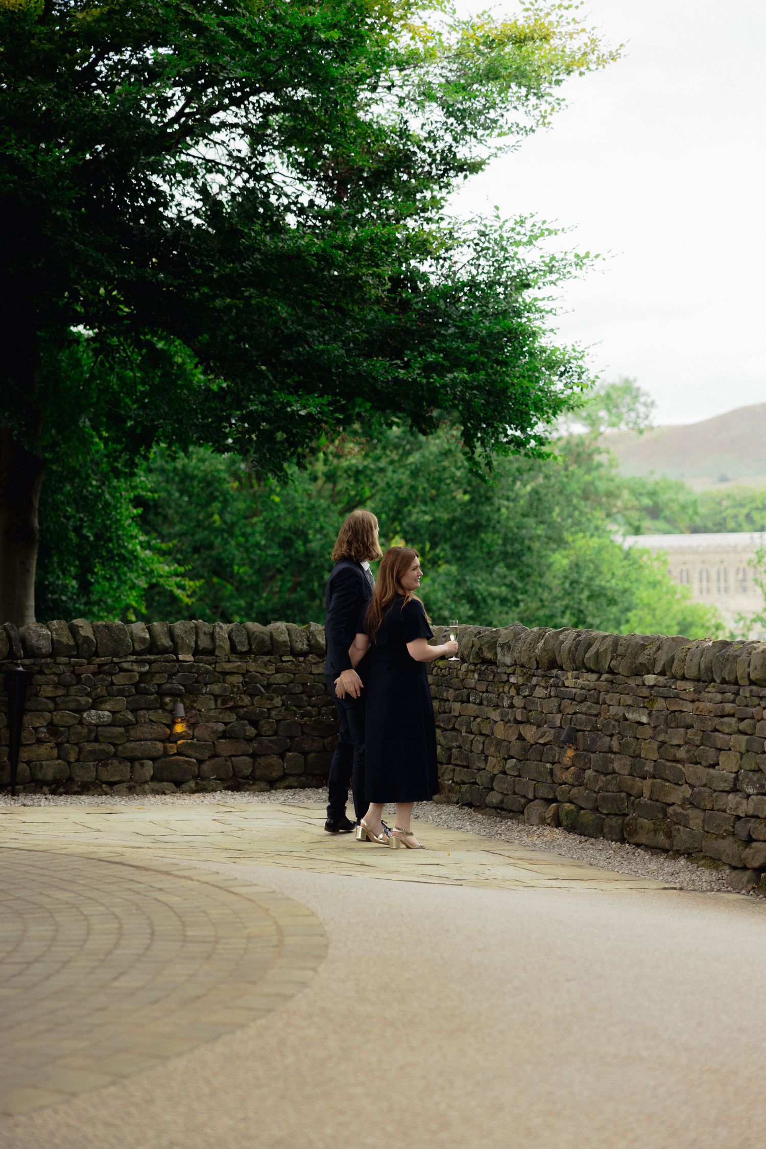 Couple shares quiet moment along stone wall overlooking scenic countryside.