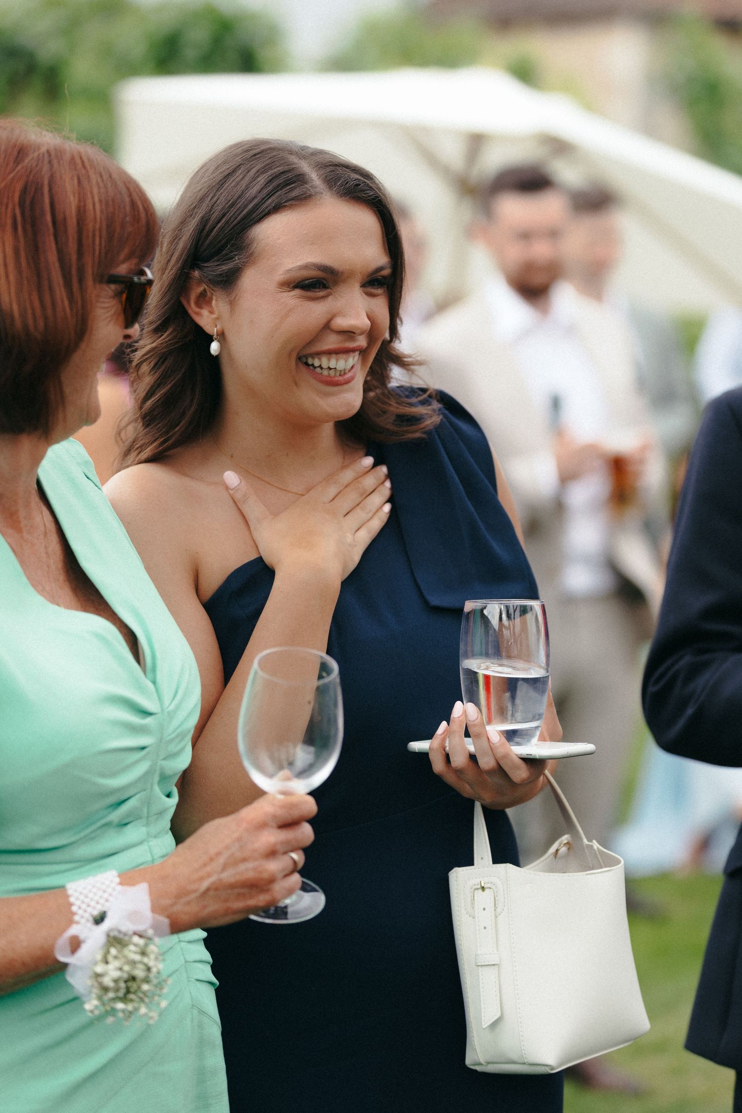 Wedding guests in mint and navy dresses sharing laughs while holding wine glasses.