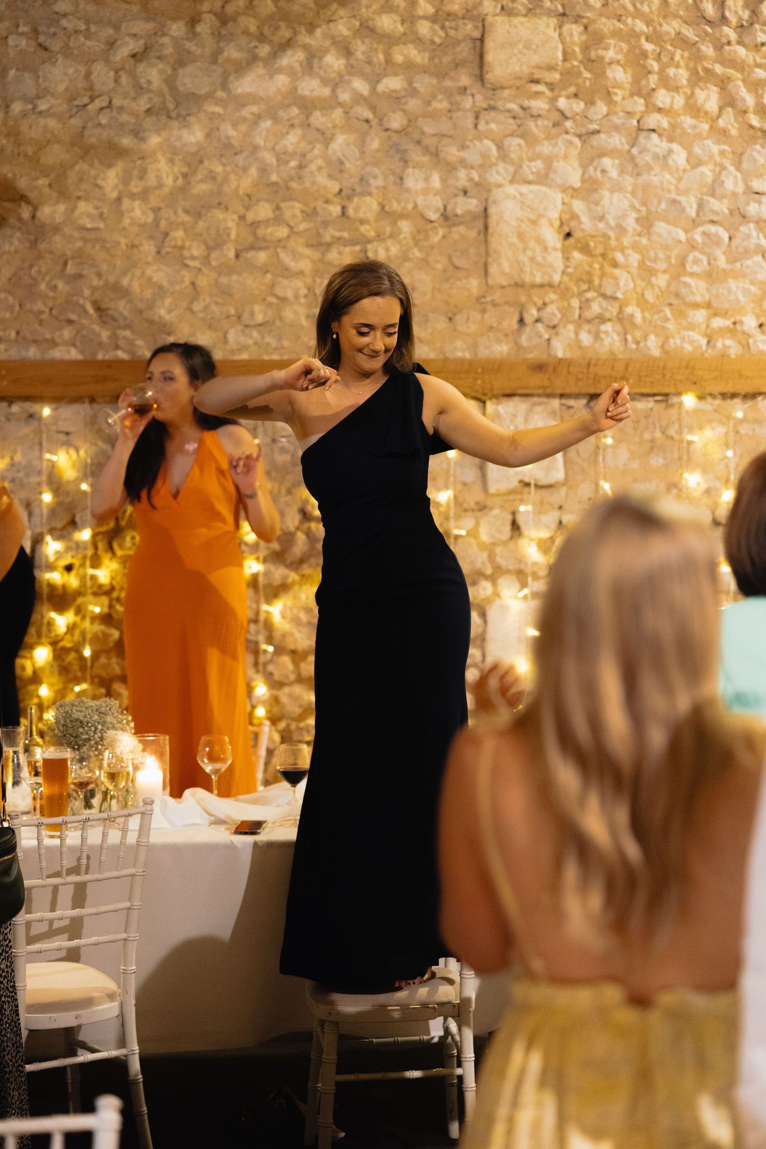 Wedding guests dancing at a rustic venue with stone walls and string lights.