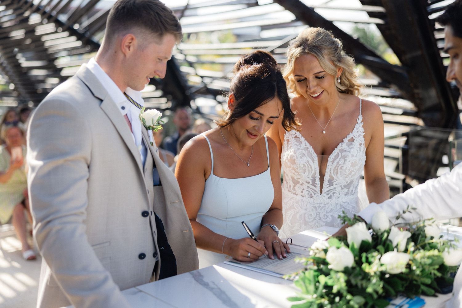 Wedding party gathered outdoors under pergola during ceremony.