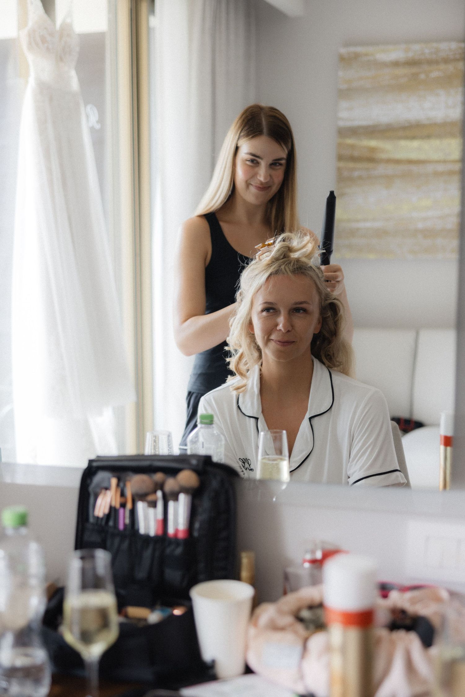 Hair stylist working on a client's hair during wedding day preparations in a bright room.