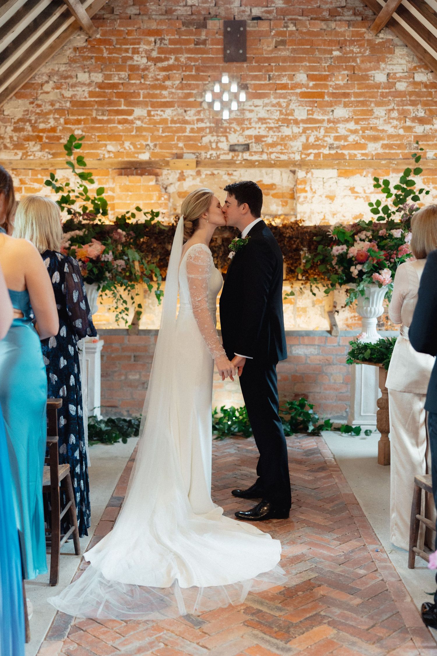 Wedding ceremony in a rustic brick room with floral decorations and guests in formal attire.