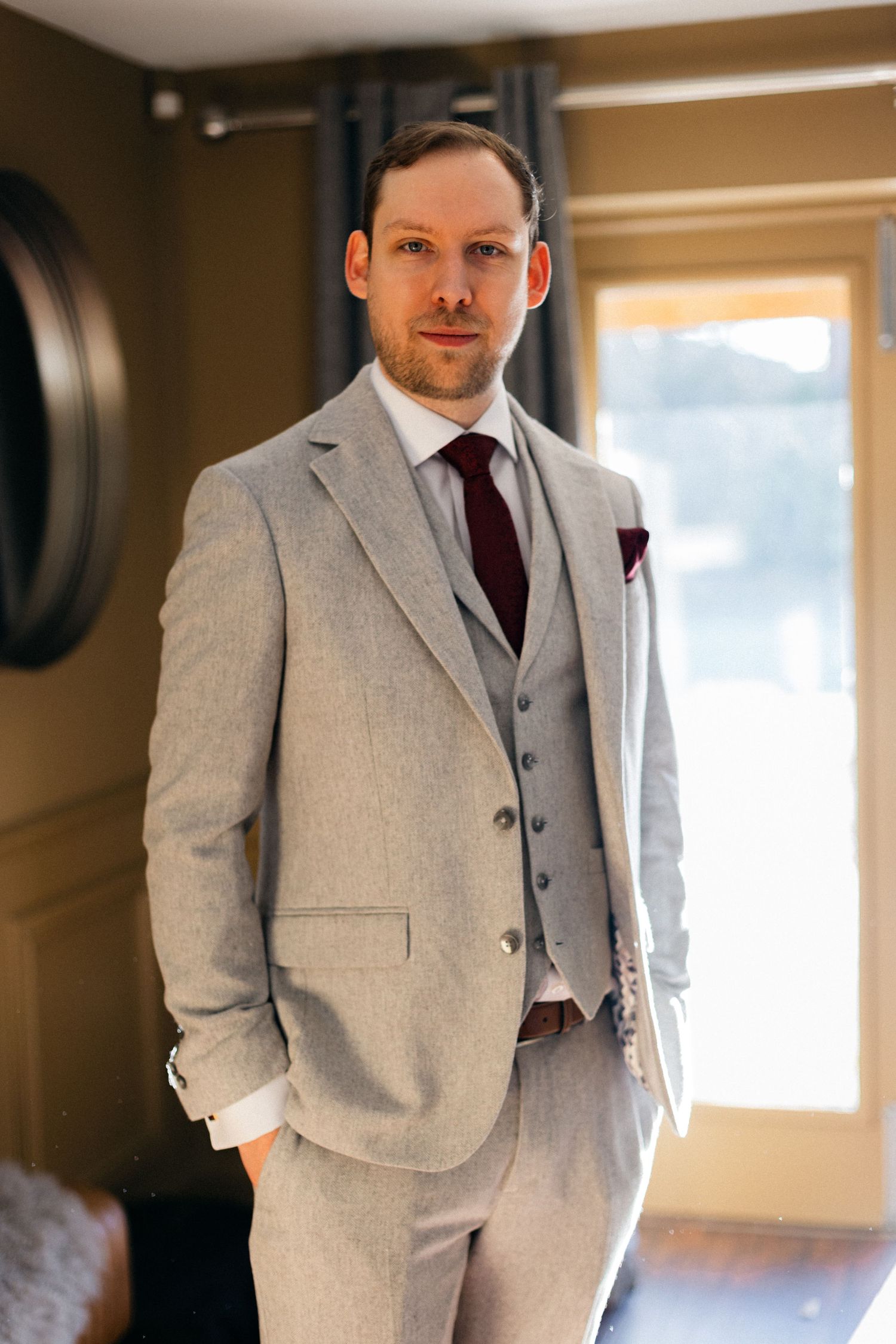 Groom wearing a tailored light grey three-piece suit with burgundy tie.