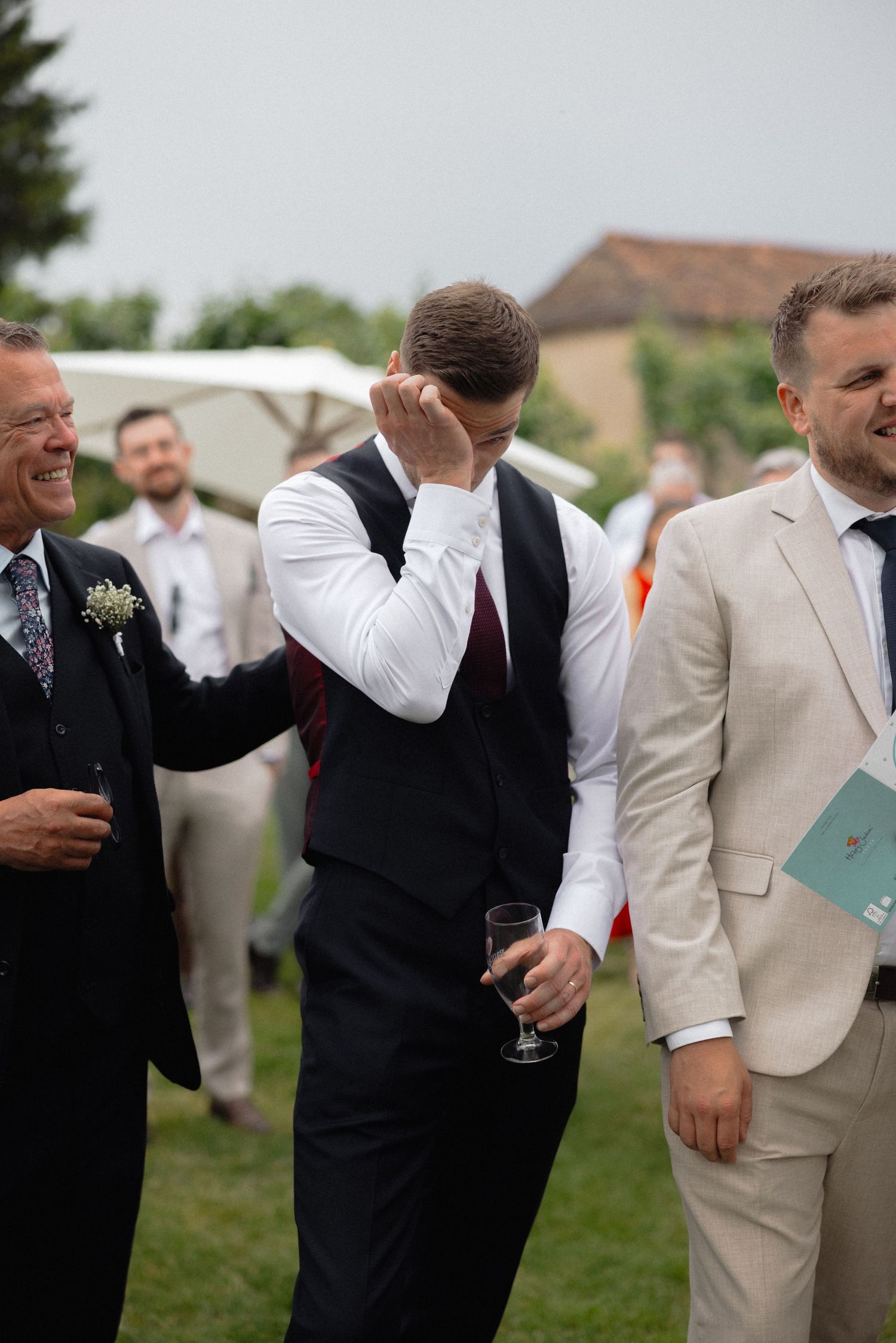 Guests in suits and formal wear socializing at outdoor wedding reception.
