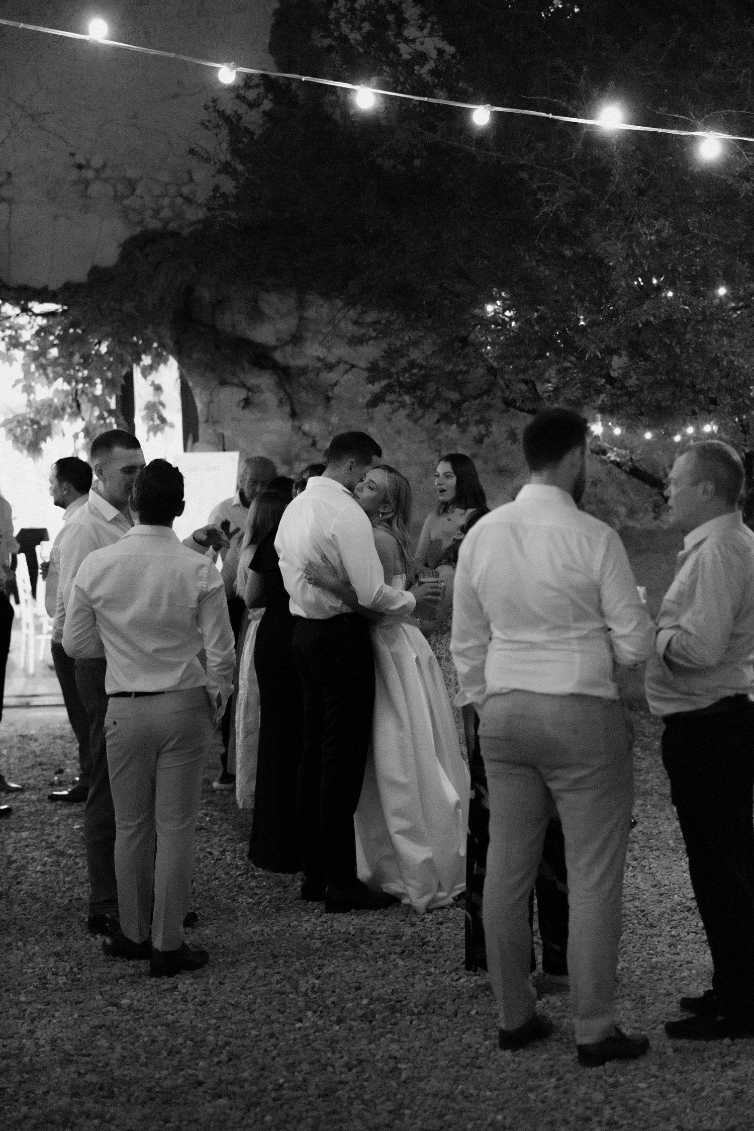 Evening wedding reception guests mingling under string lights in black and white.
