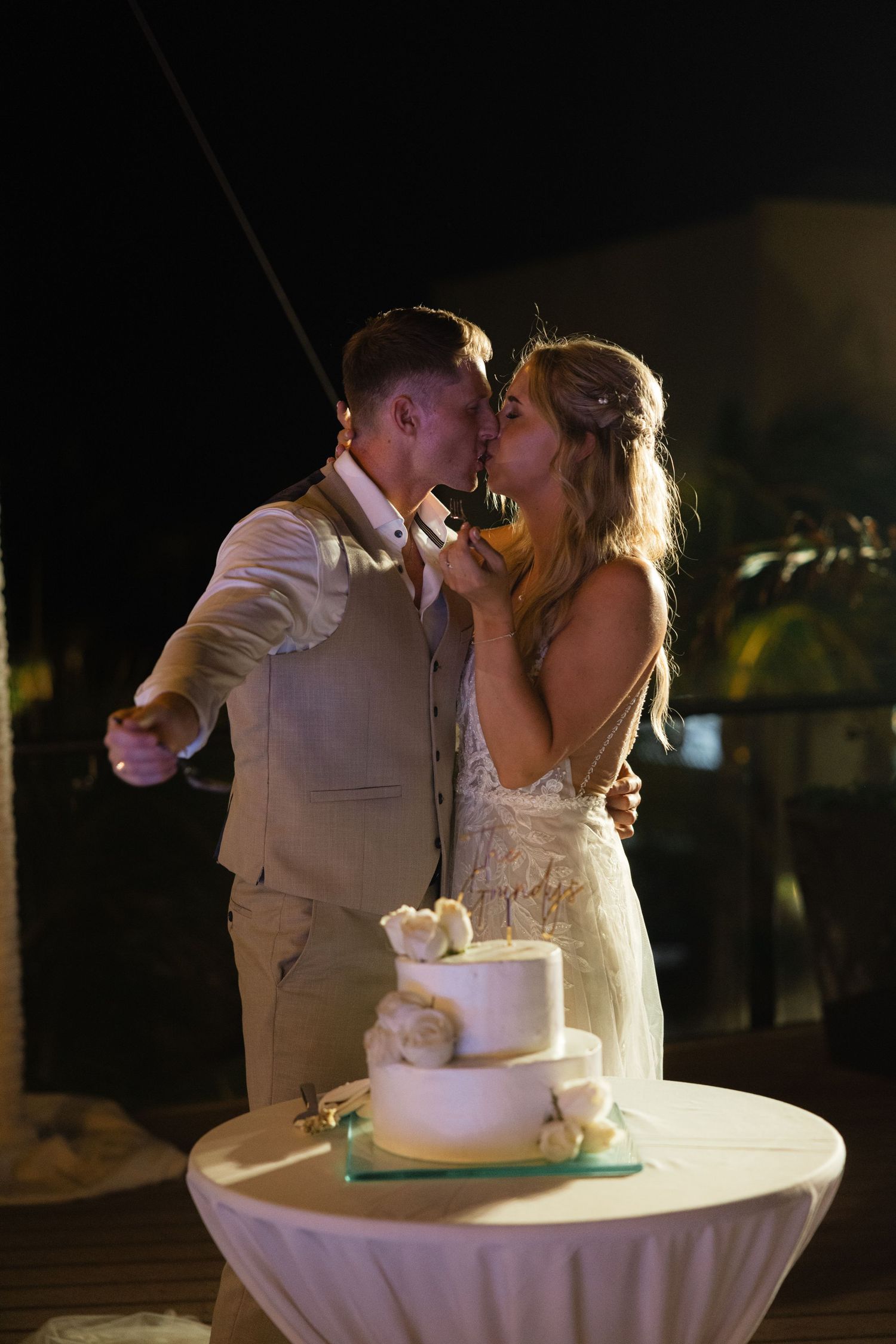 Romantic moment between newlyweds sharing cake beside their elegant white tiered wedding cake.