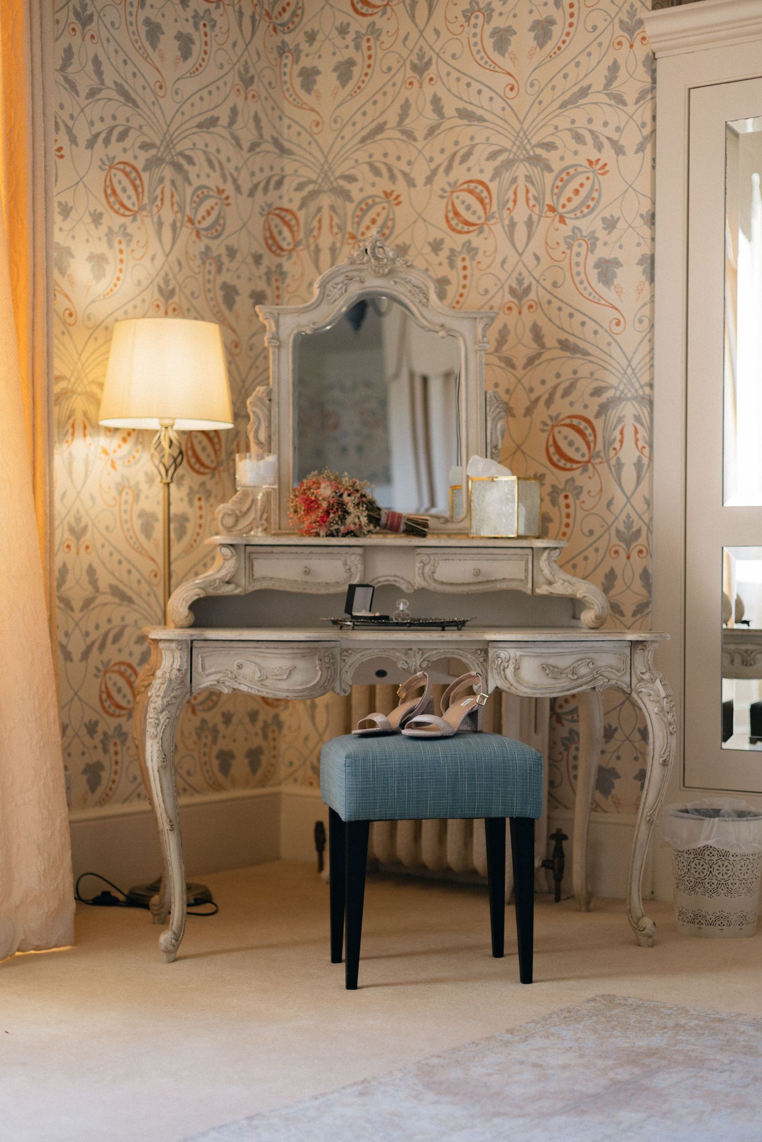 Vintage-style vanity table with ornate mirror against floral wallpaper in bridal suite.
