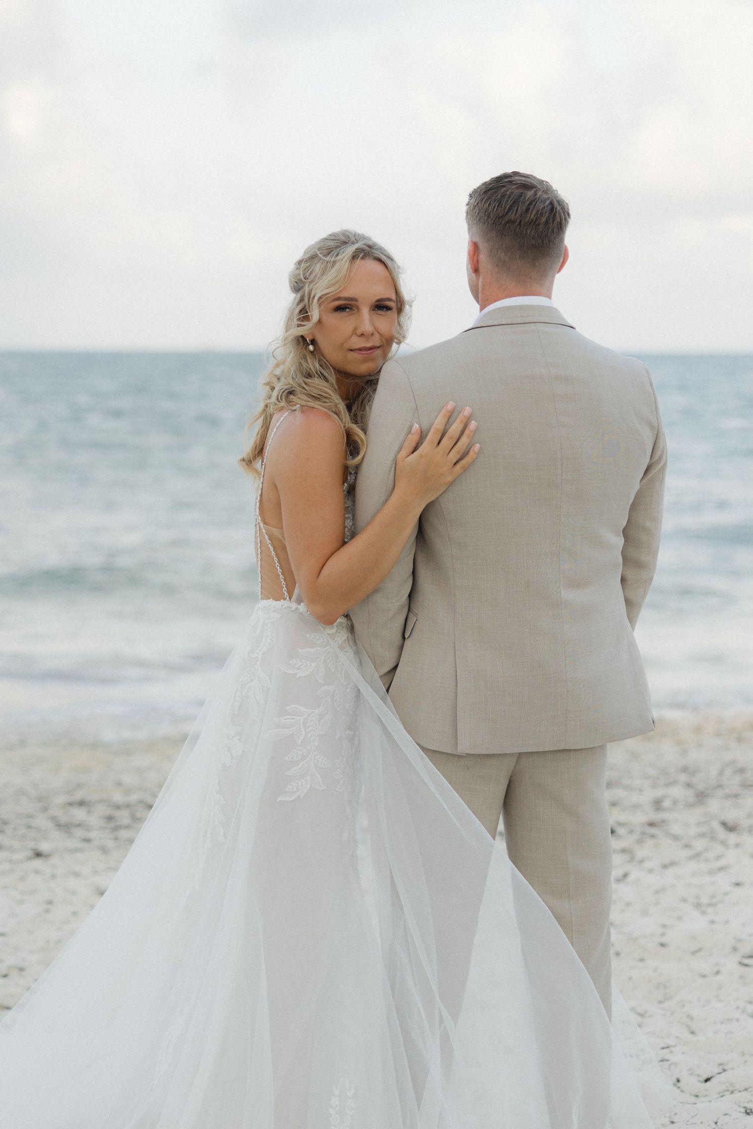 Romantic beach wedding photos showing a couple in white dress and beige suit against an ocean backdrop.