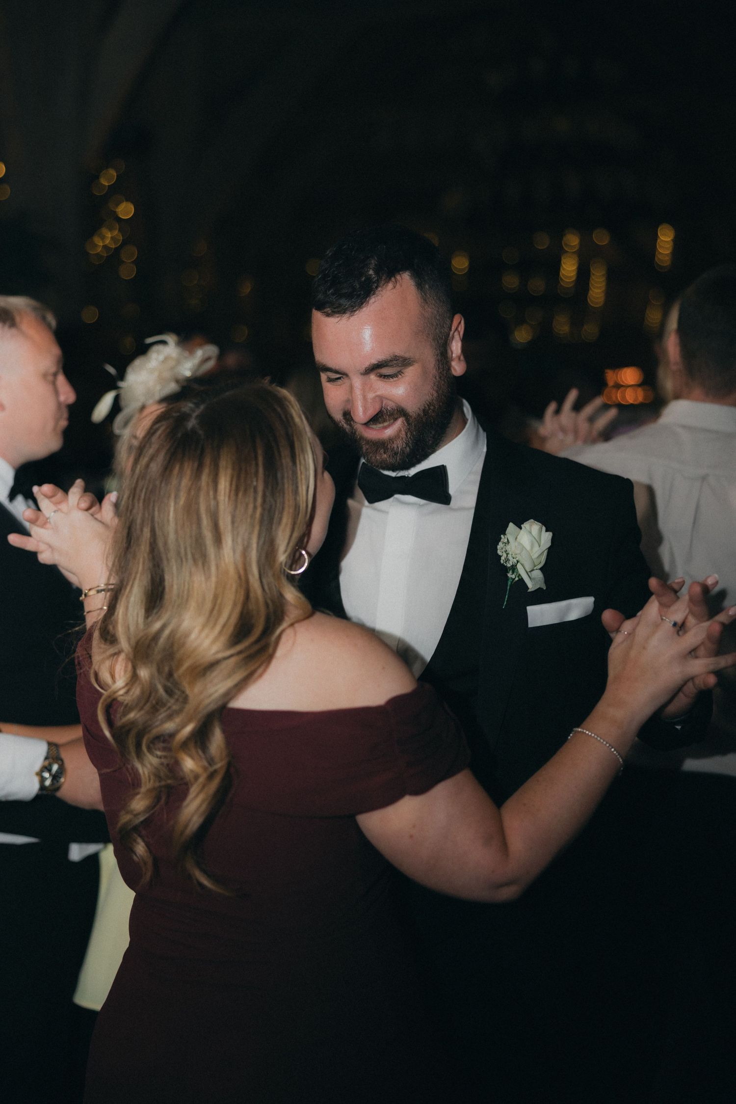 A couple dances together at an elegant wedding reception with warm lighting in the background.