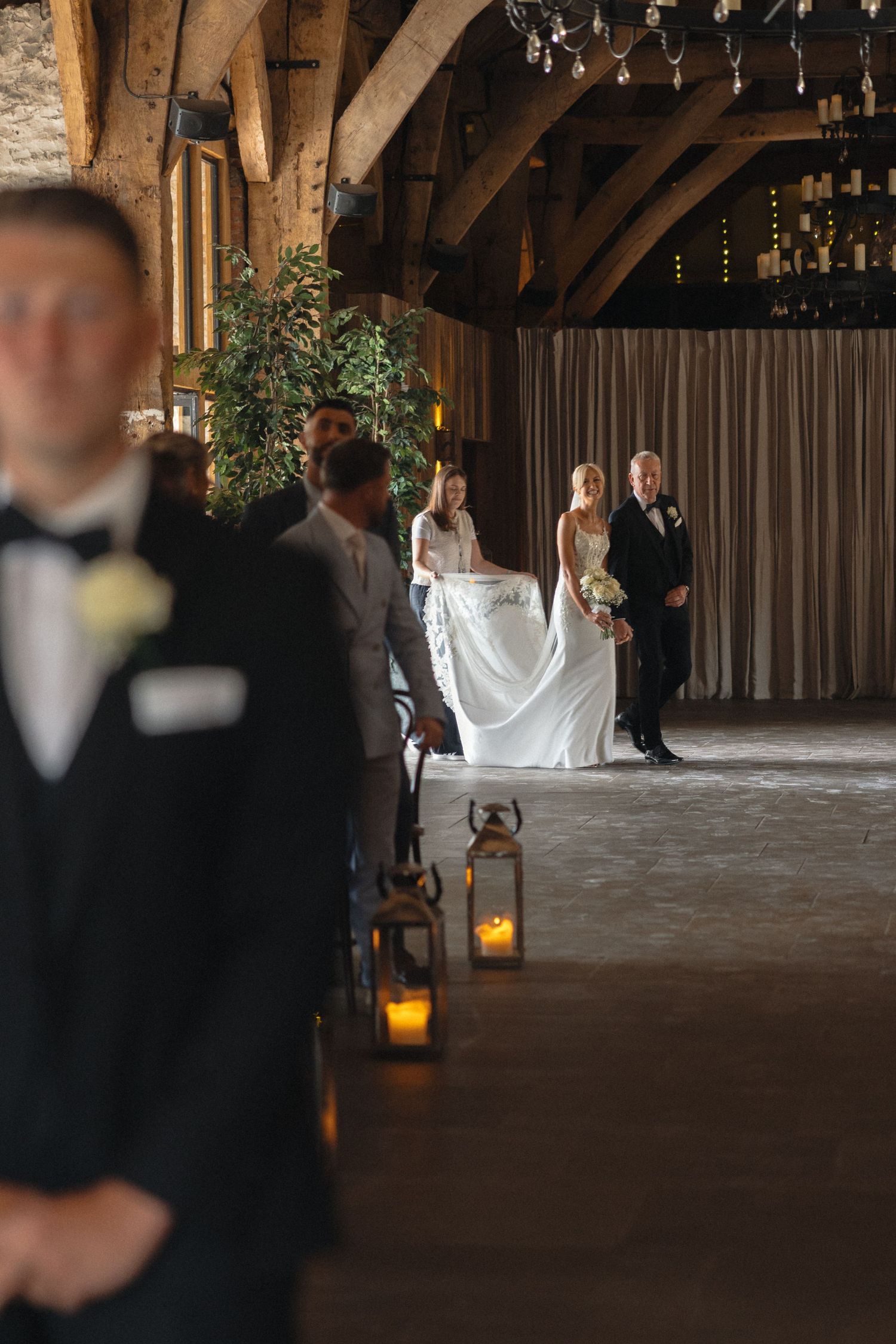 Wedding ceremony in progress inside a rustic barn venue with hanging lanterns.