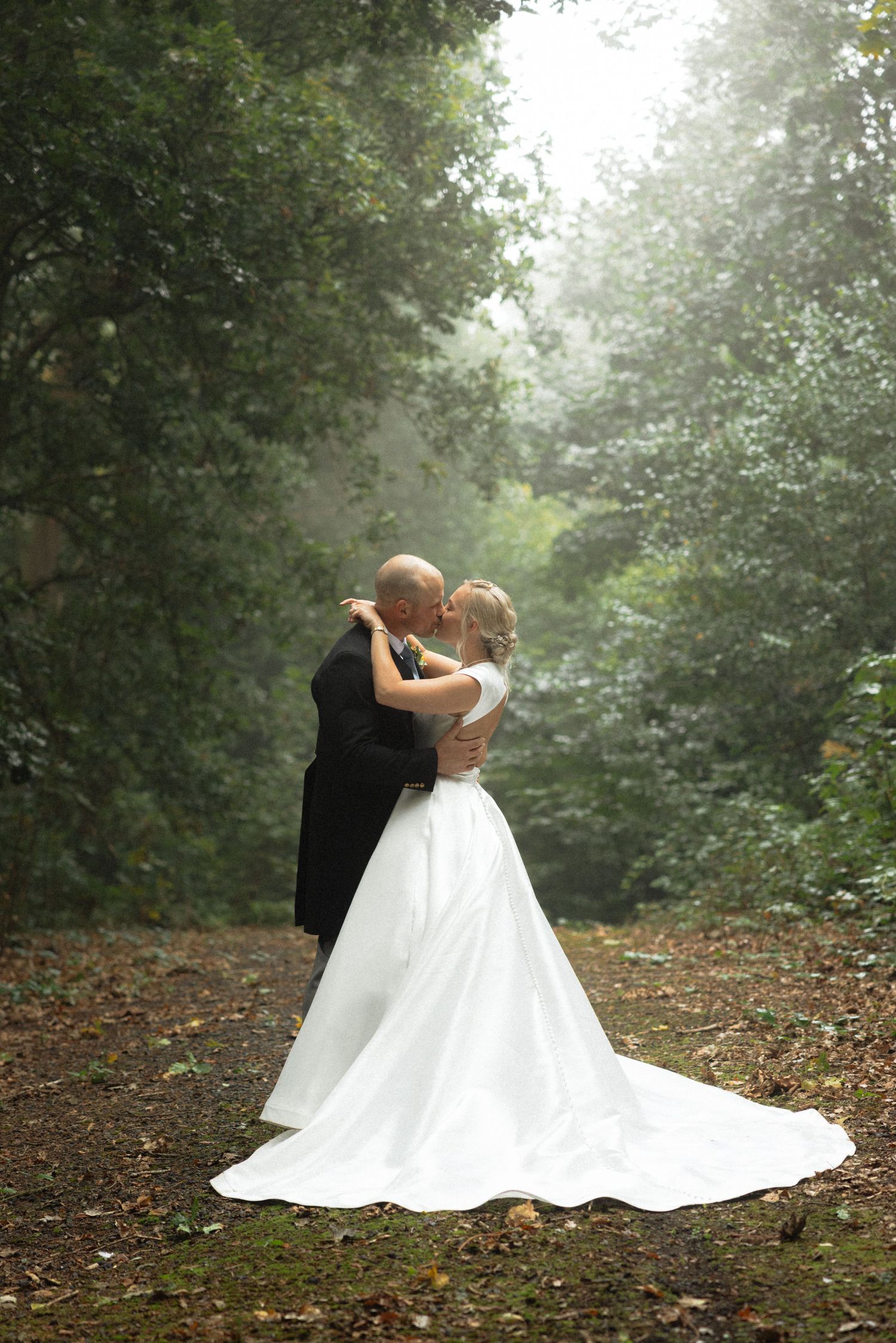 Romantic wedding couple embraces in a dreamy forest setting with flowing white dress.