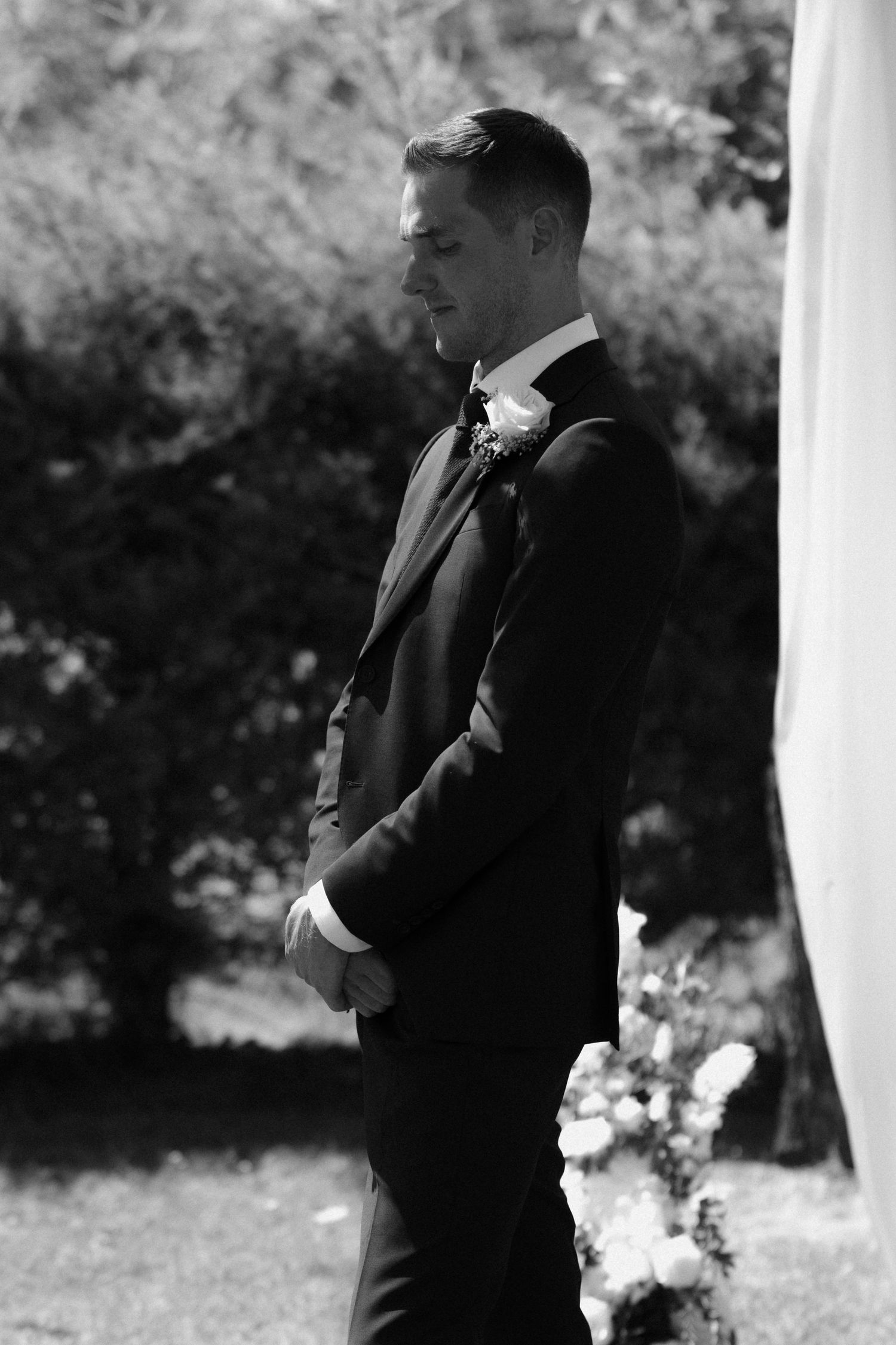 Black and white photo of groomsmen standing under white outdoor wedding canopy.