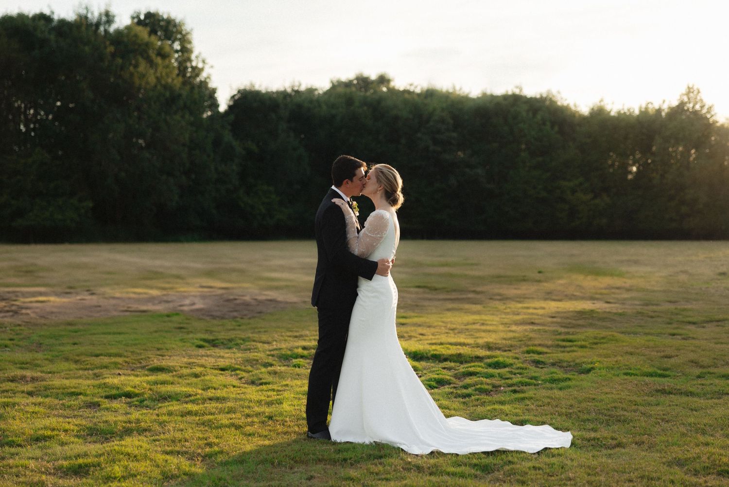Silhouettes of a couple in formal attire walking across a sunlit field at golden hour.