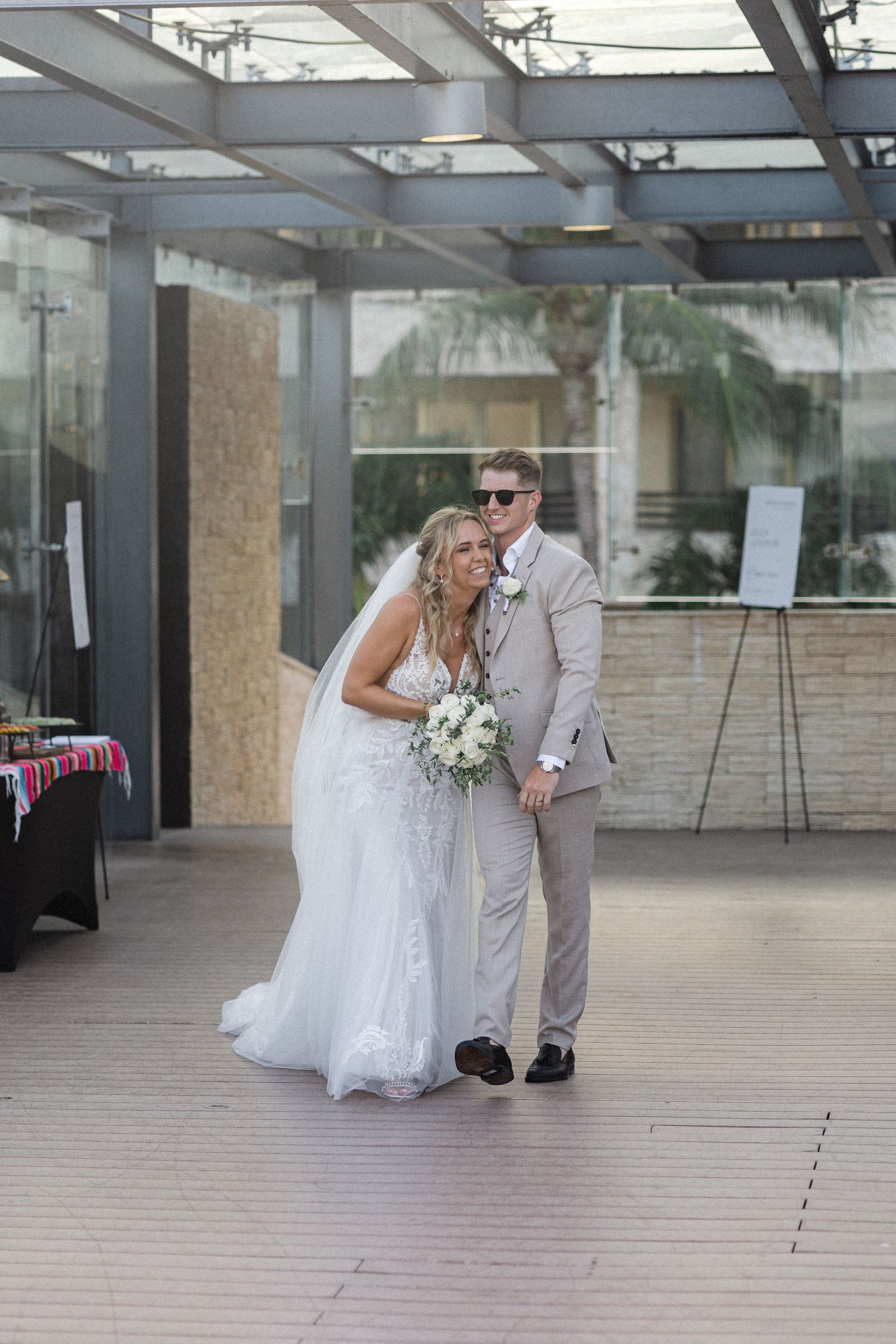Couple walks through modern glass-enclosed venue space during wedding celebration.
