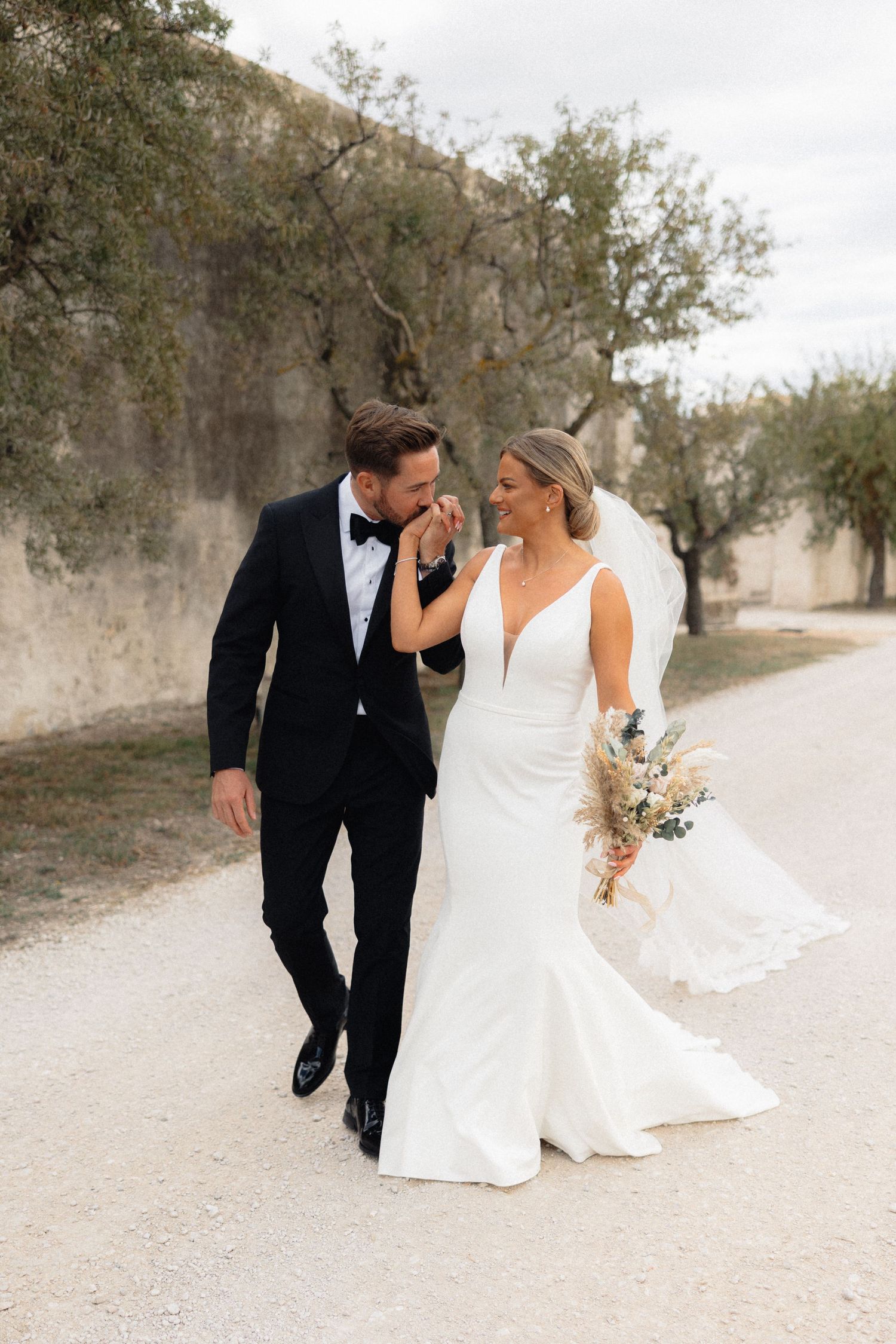 Wedding couple walking and laughing together on a rustic path lined with trees.