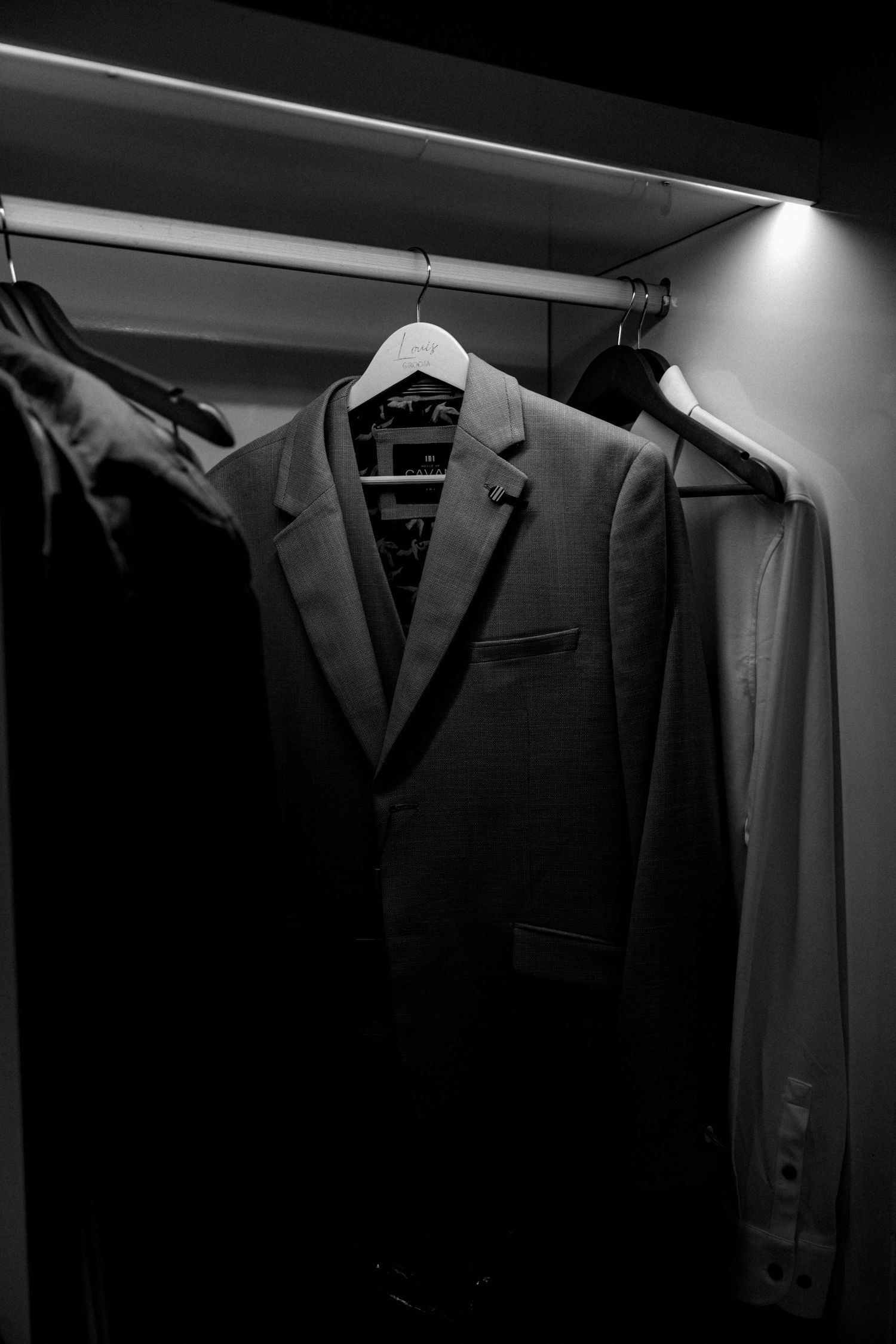 Dark suit jacket hanging in closet with dramatic lighting.