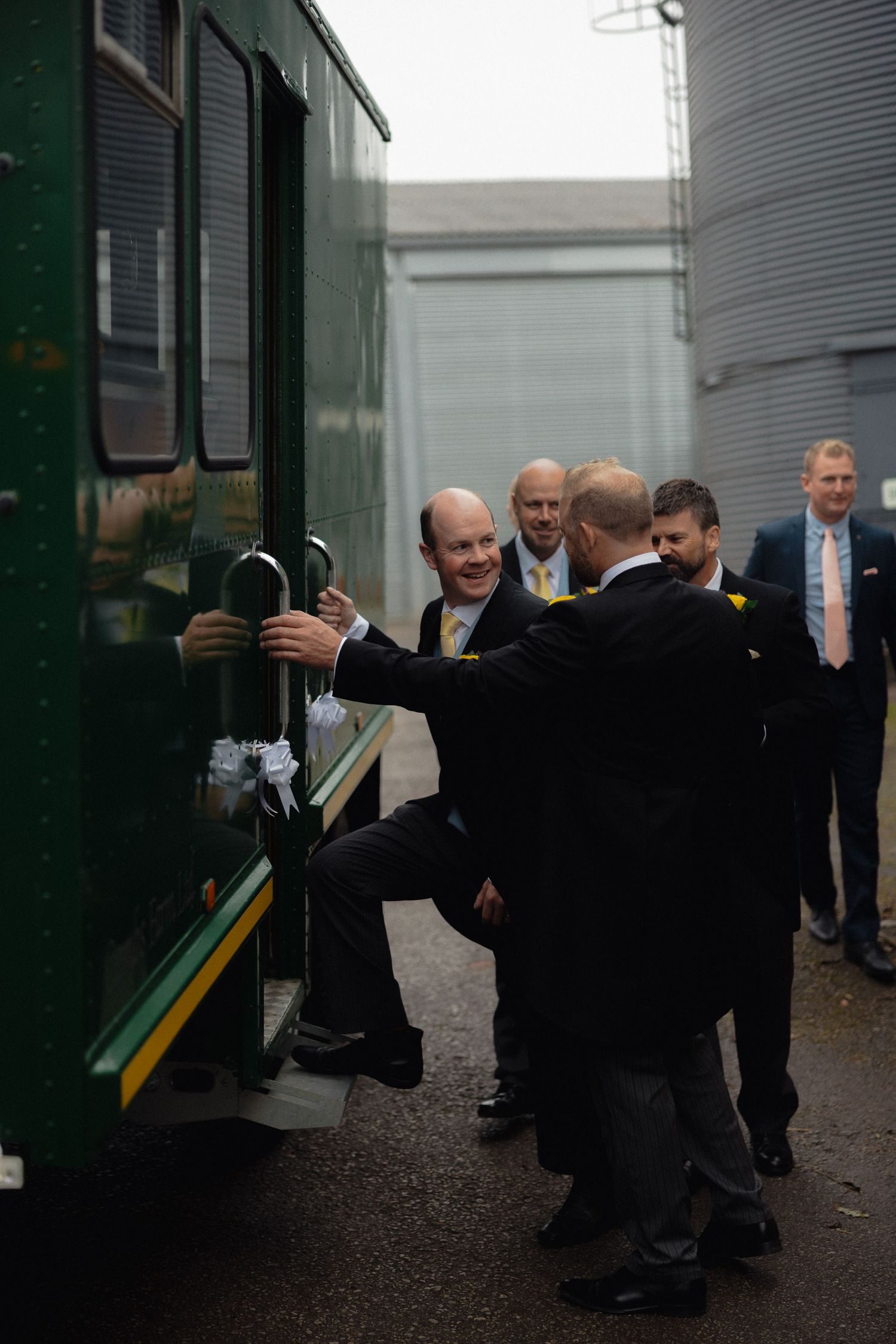Group of people in formal attire interacting outside a green vehicle.