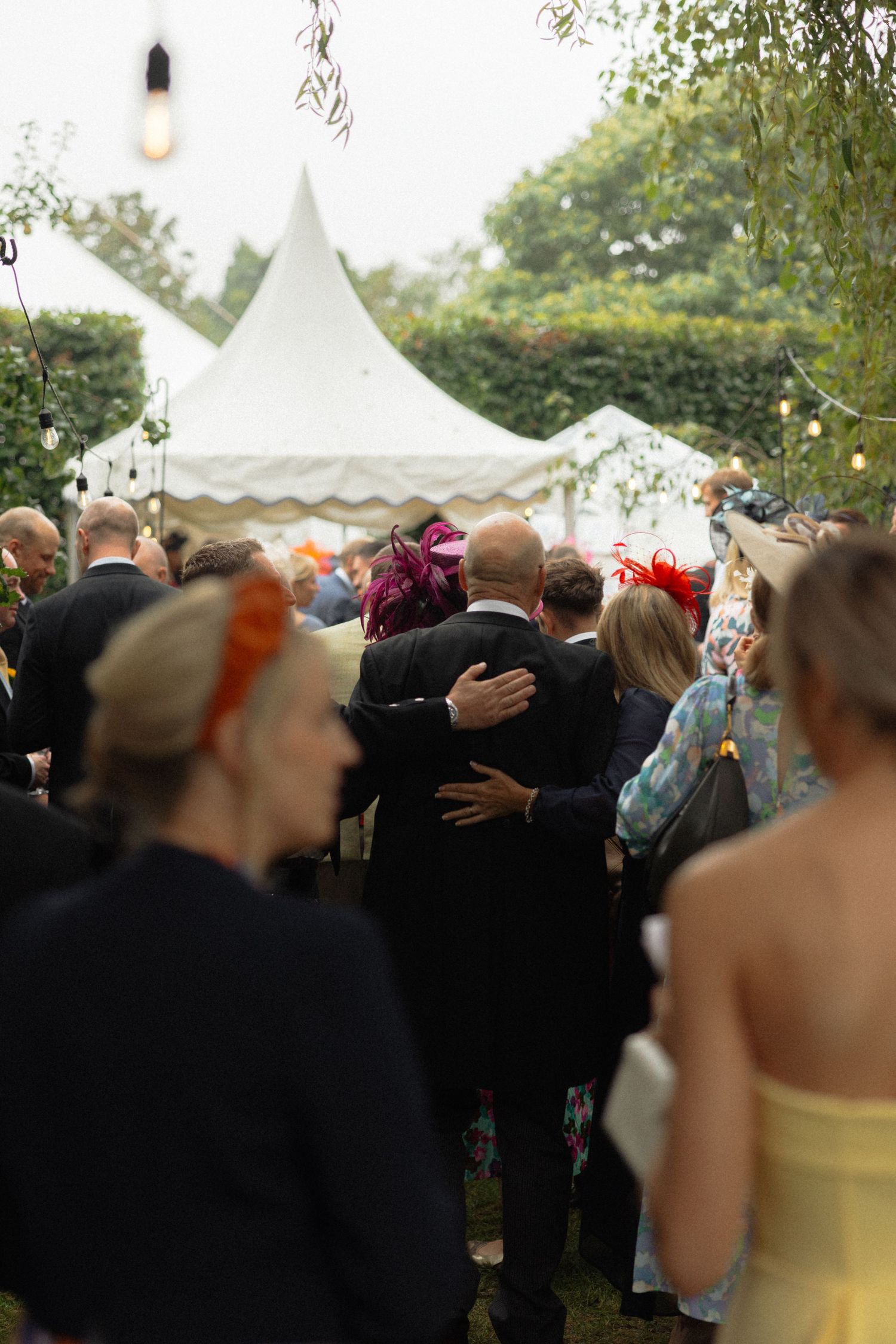 Wedding guests gathered under white tents during an outdoor celebration.