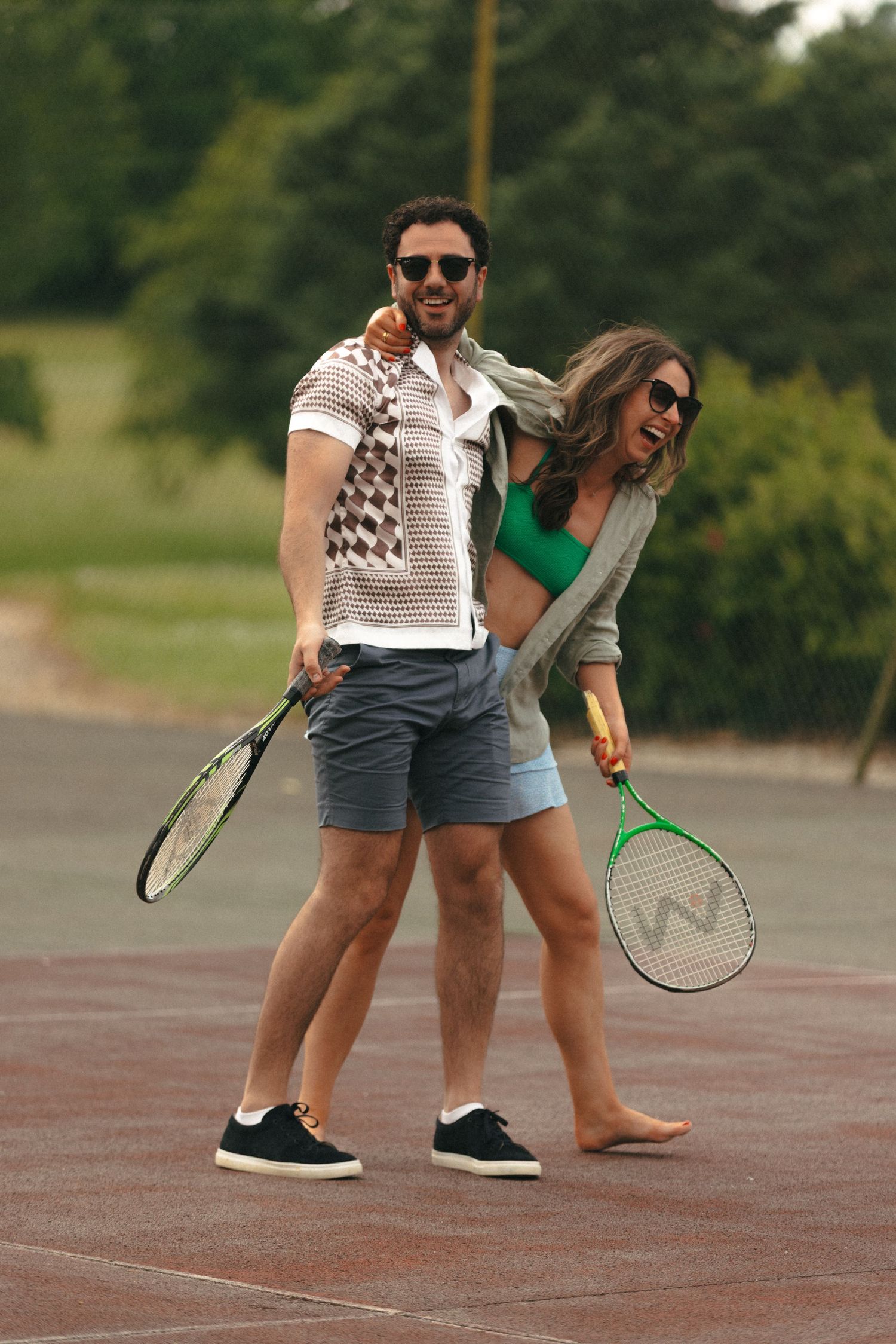 Two tennis players in casual attire standing together on a court holding racquets.