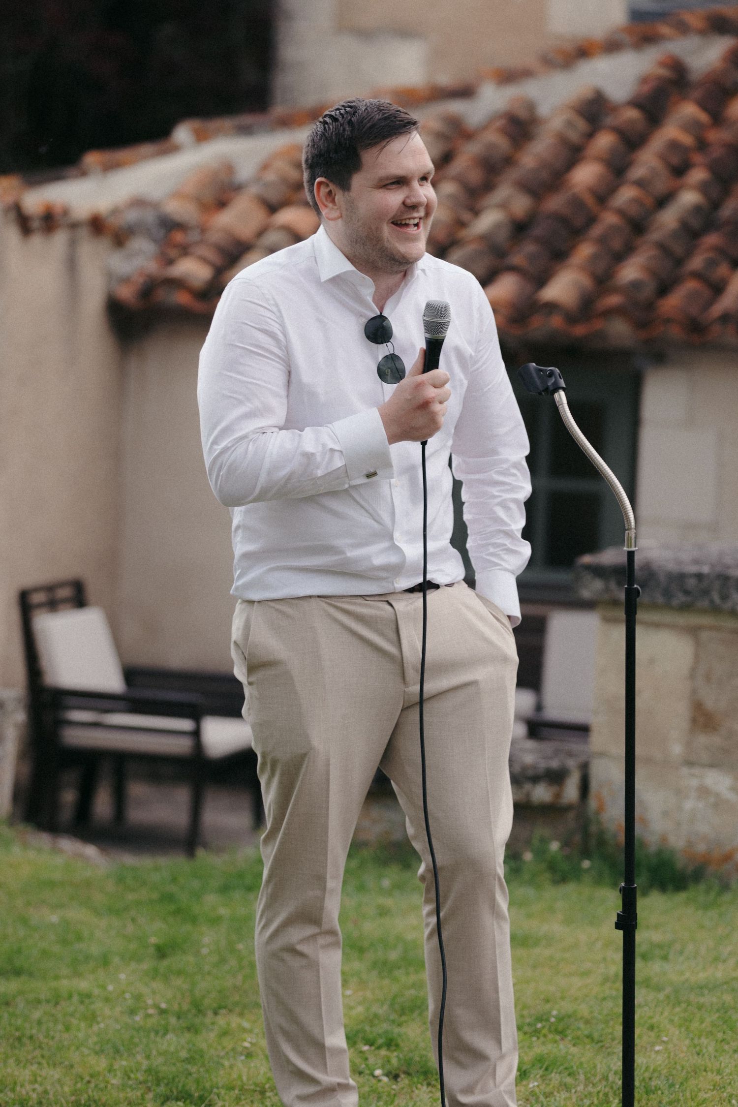Man in white shirt and khaki pants speaks into microphone at outdoor event.
