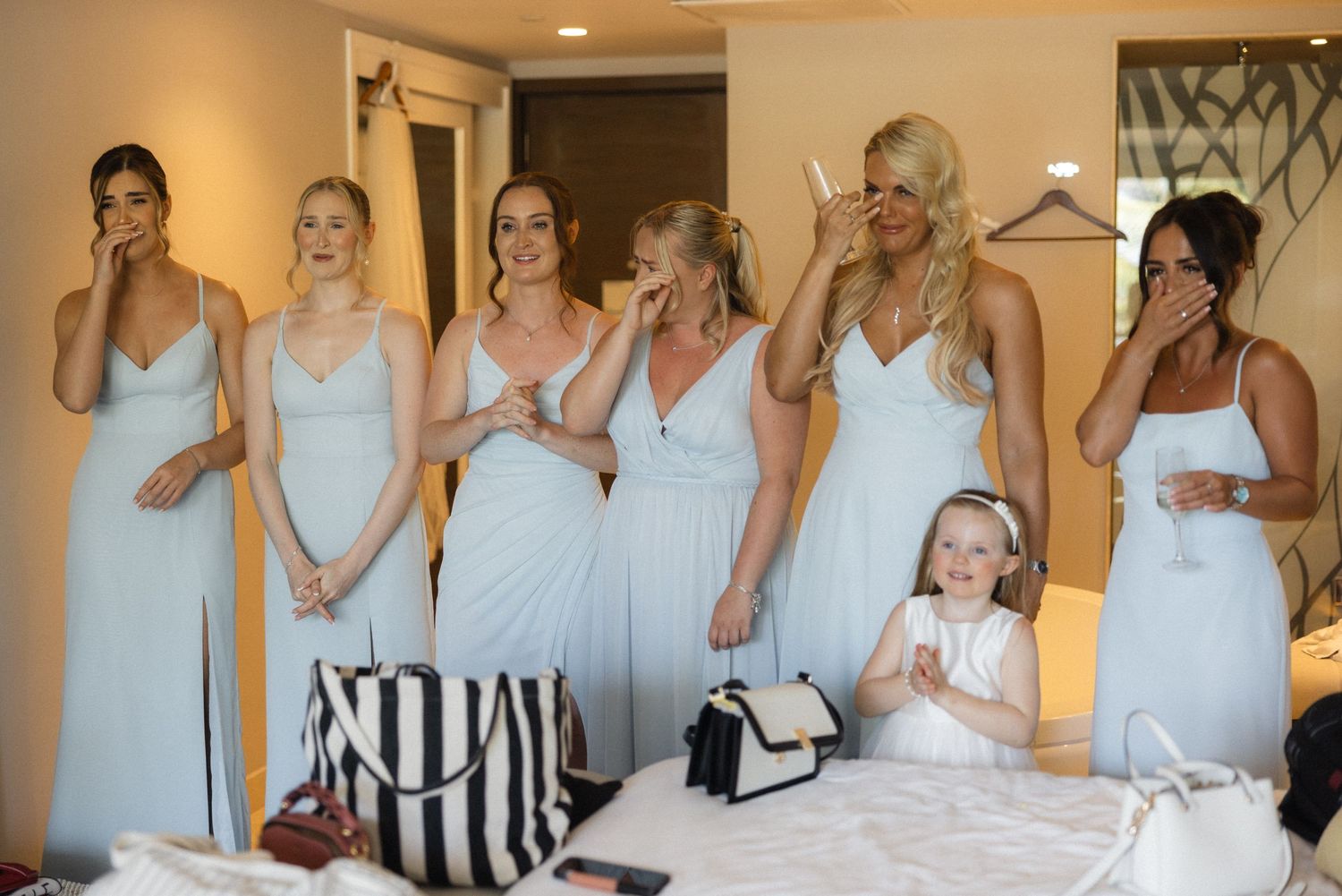 Bridesmaids in coordinated pale blue attire share excited moments together.
