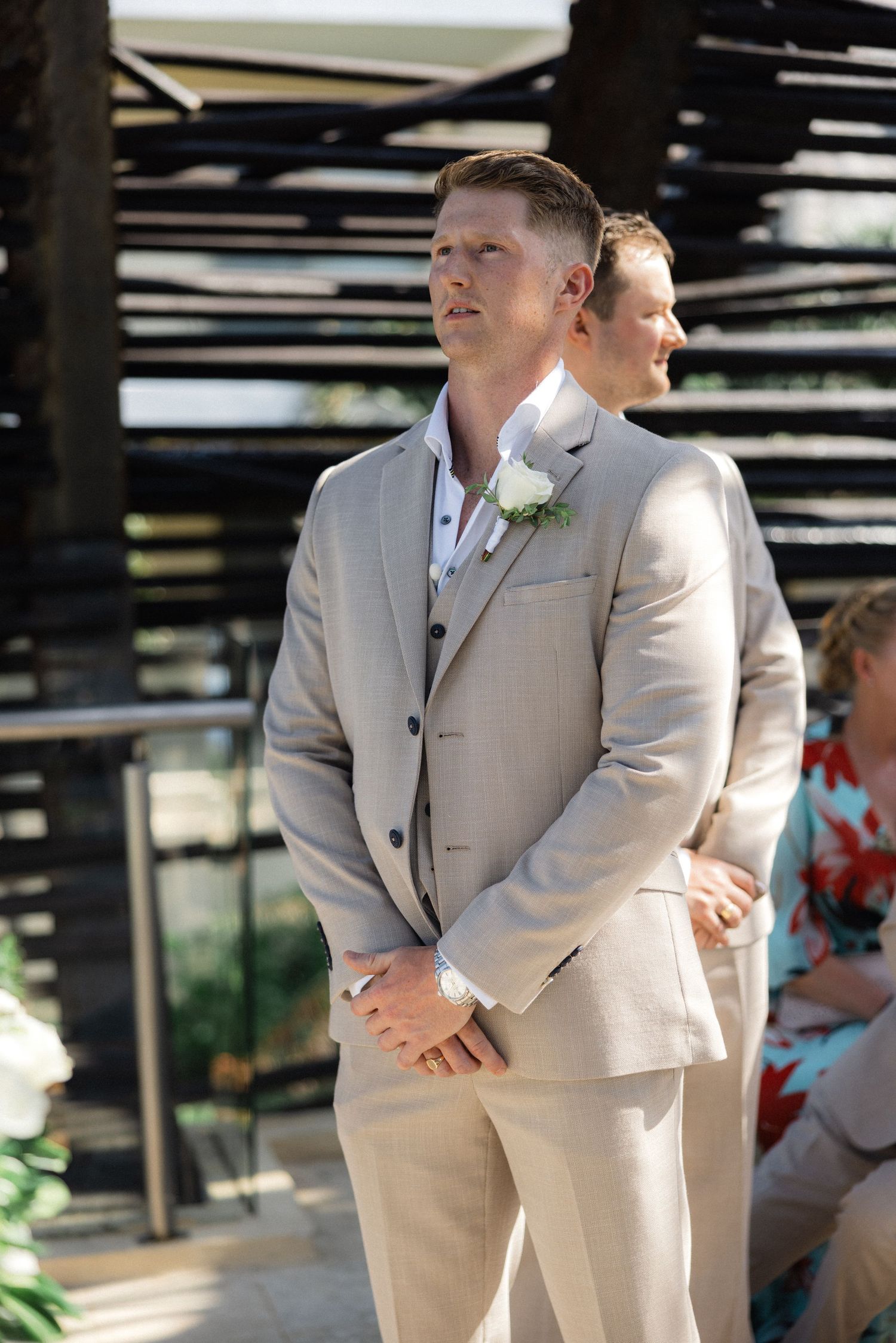 Groomsmen in beige suits standing together during an outdoor wedding ceremony.