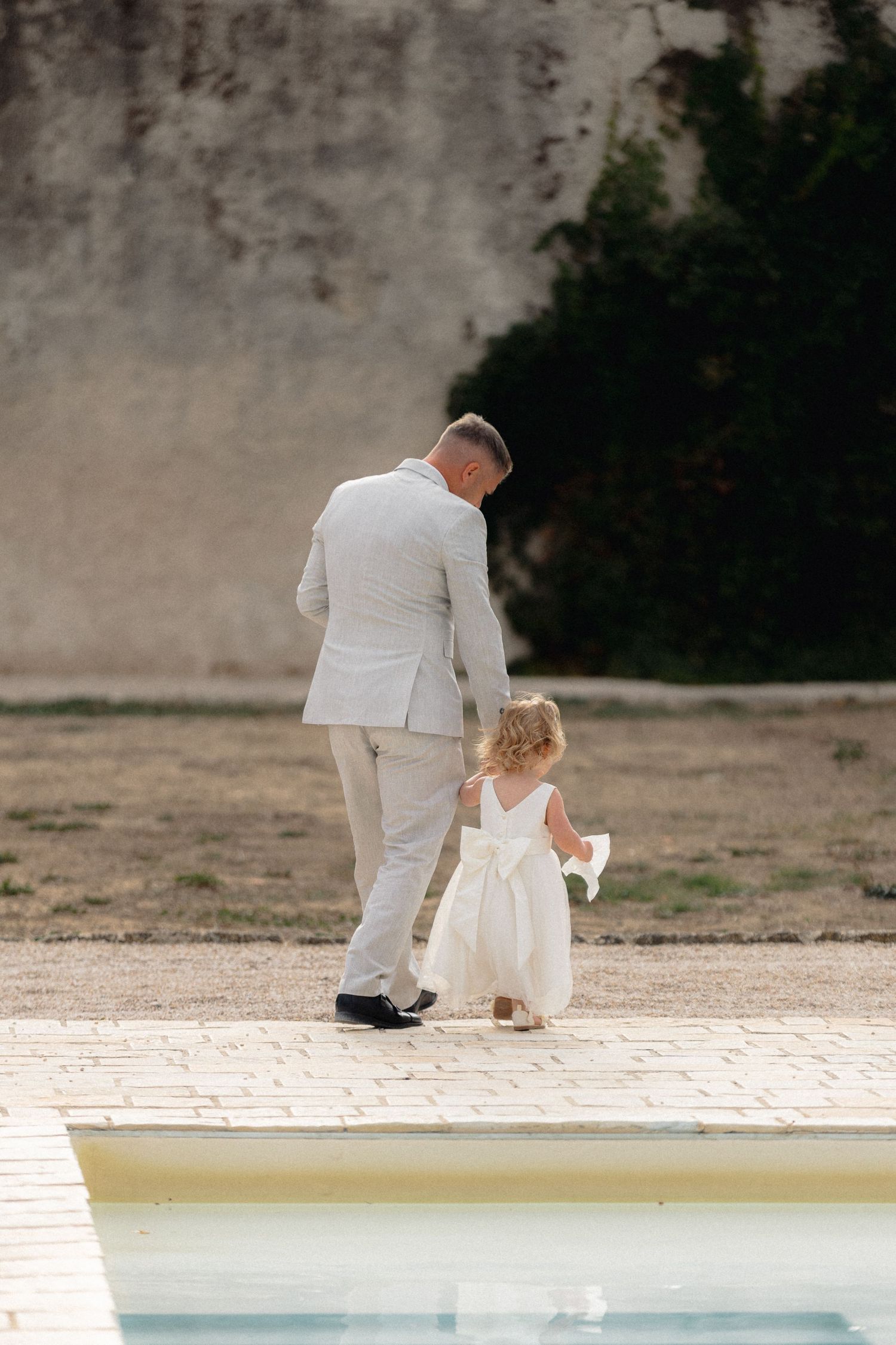 Elegant couple in white formal wear walking near a serene pool setting.