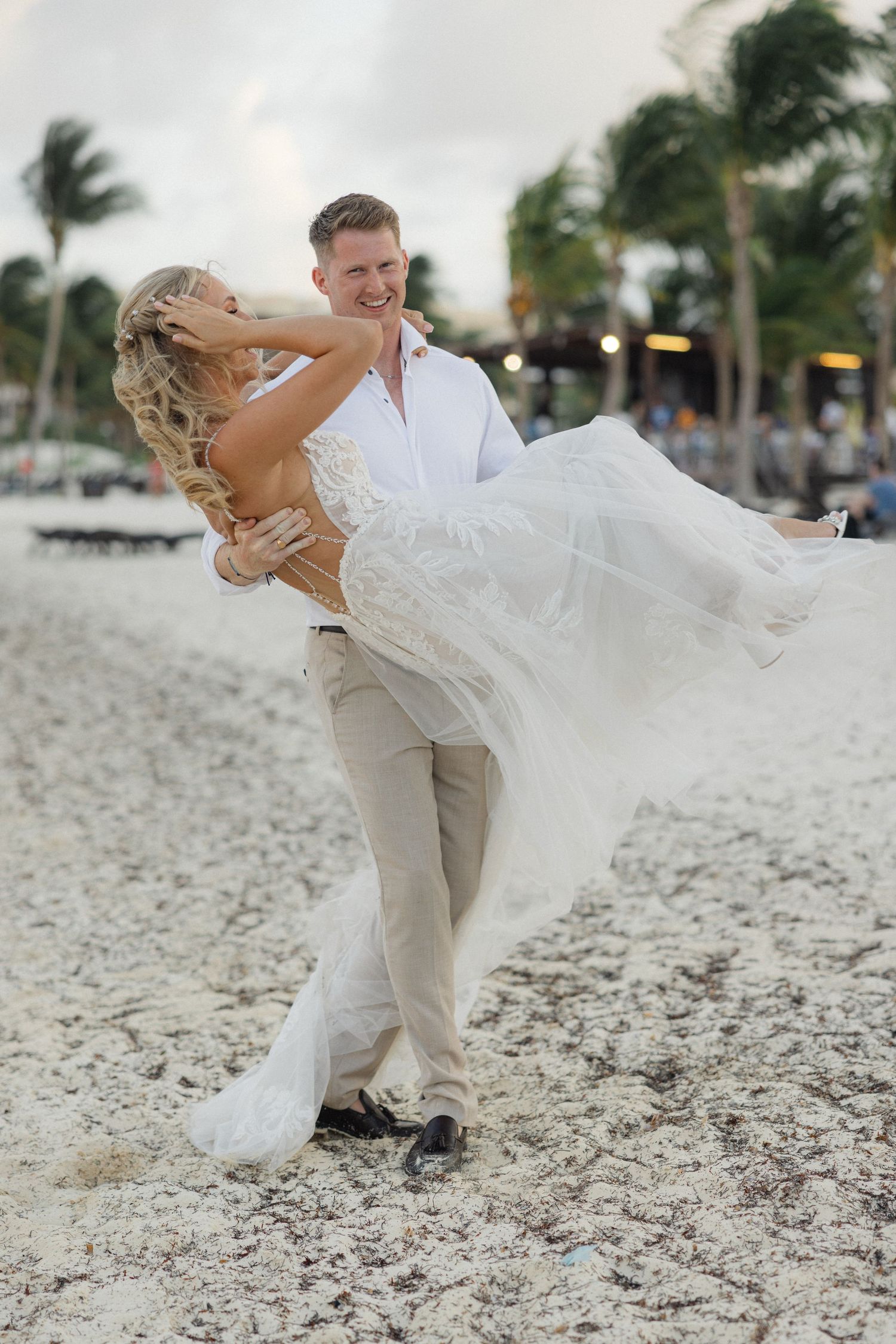 Romantic beach wedding sequence captures playful dip poses on sandy shoreline.