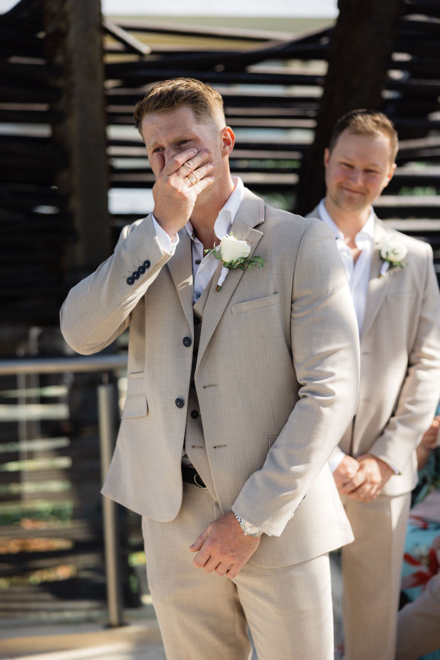 Groomsmen in matching beige suits standing together at outdoor venue.
