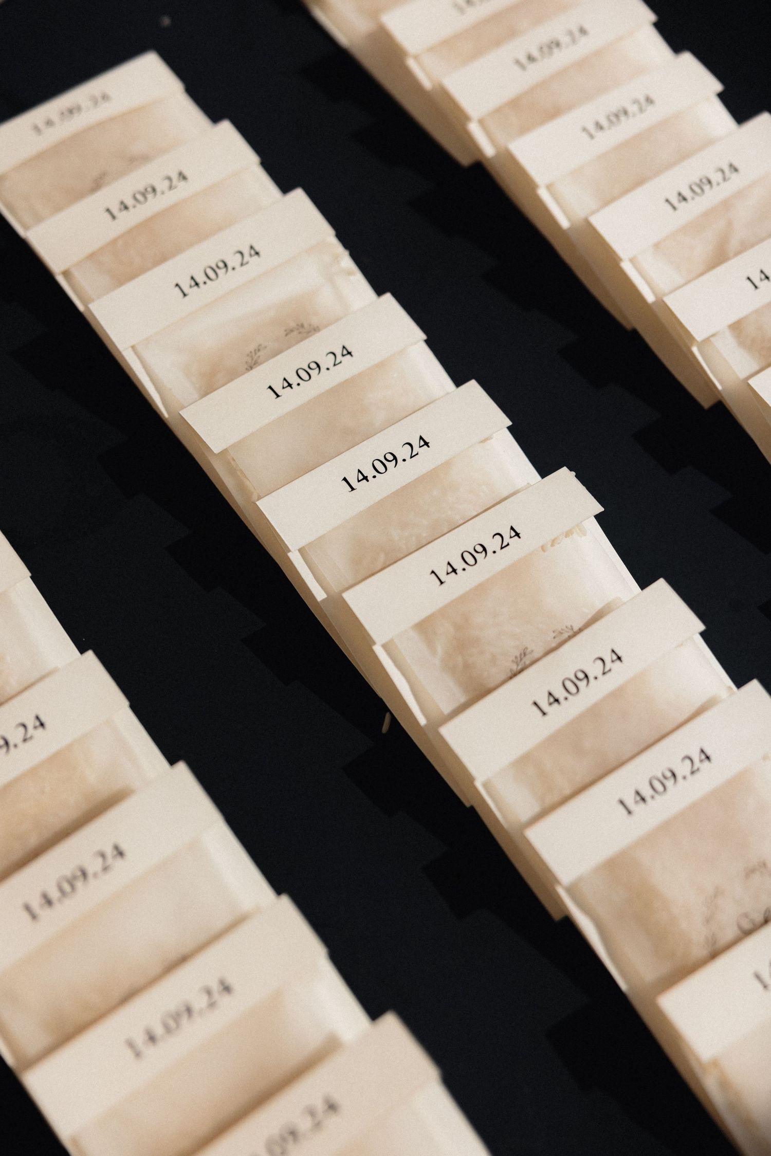 Row of cream colored wedding escort cards arranged diagonally on dark surface.
