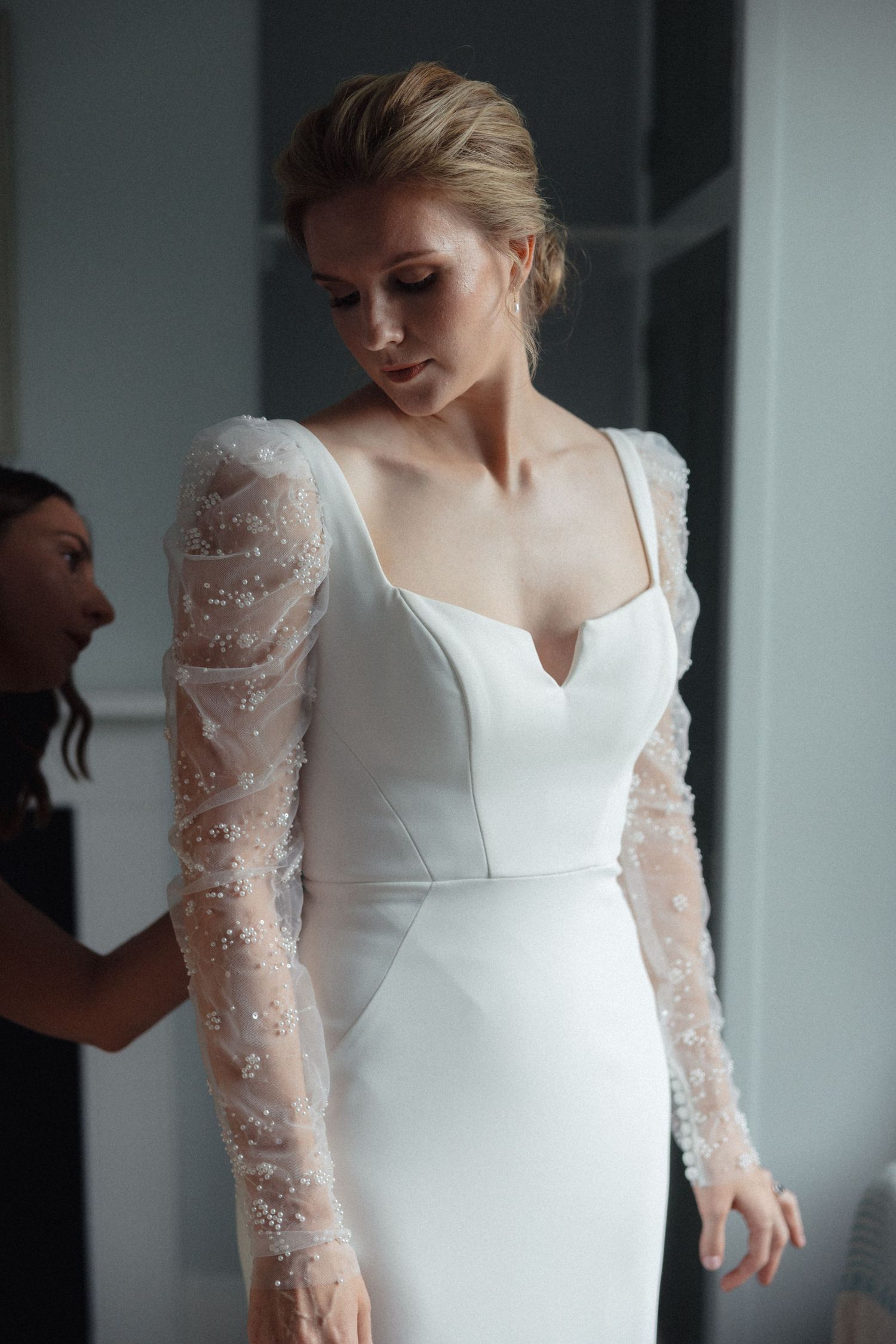 Elegant white wedding dress with detailed lace sleeves being fitted.
