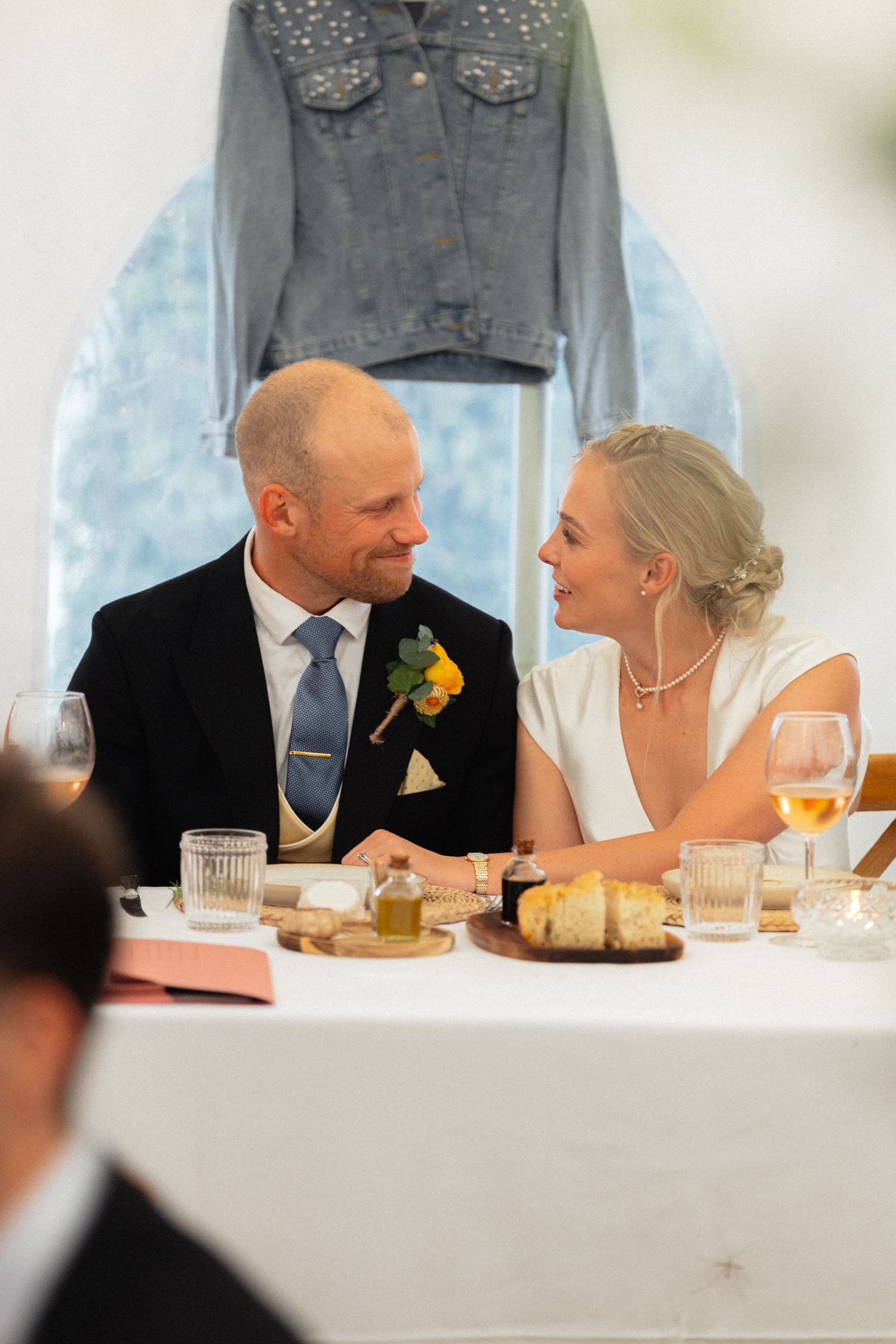 Couple shares intimate moment at wedding reception table with decorative lights overhead.