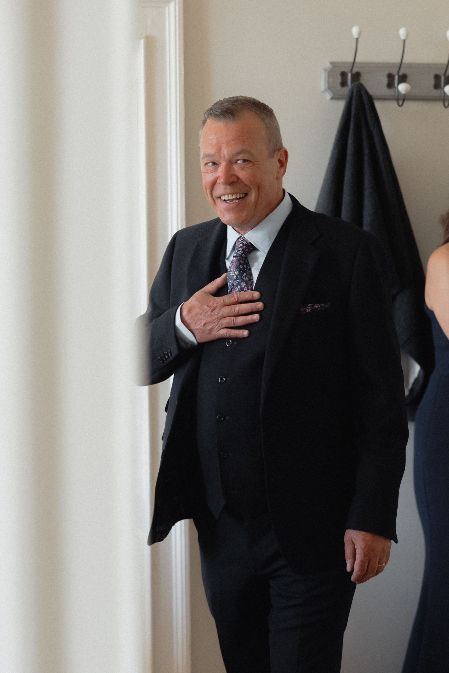 Man in formal attire smiling warmly in a bright indoor setting.