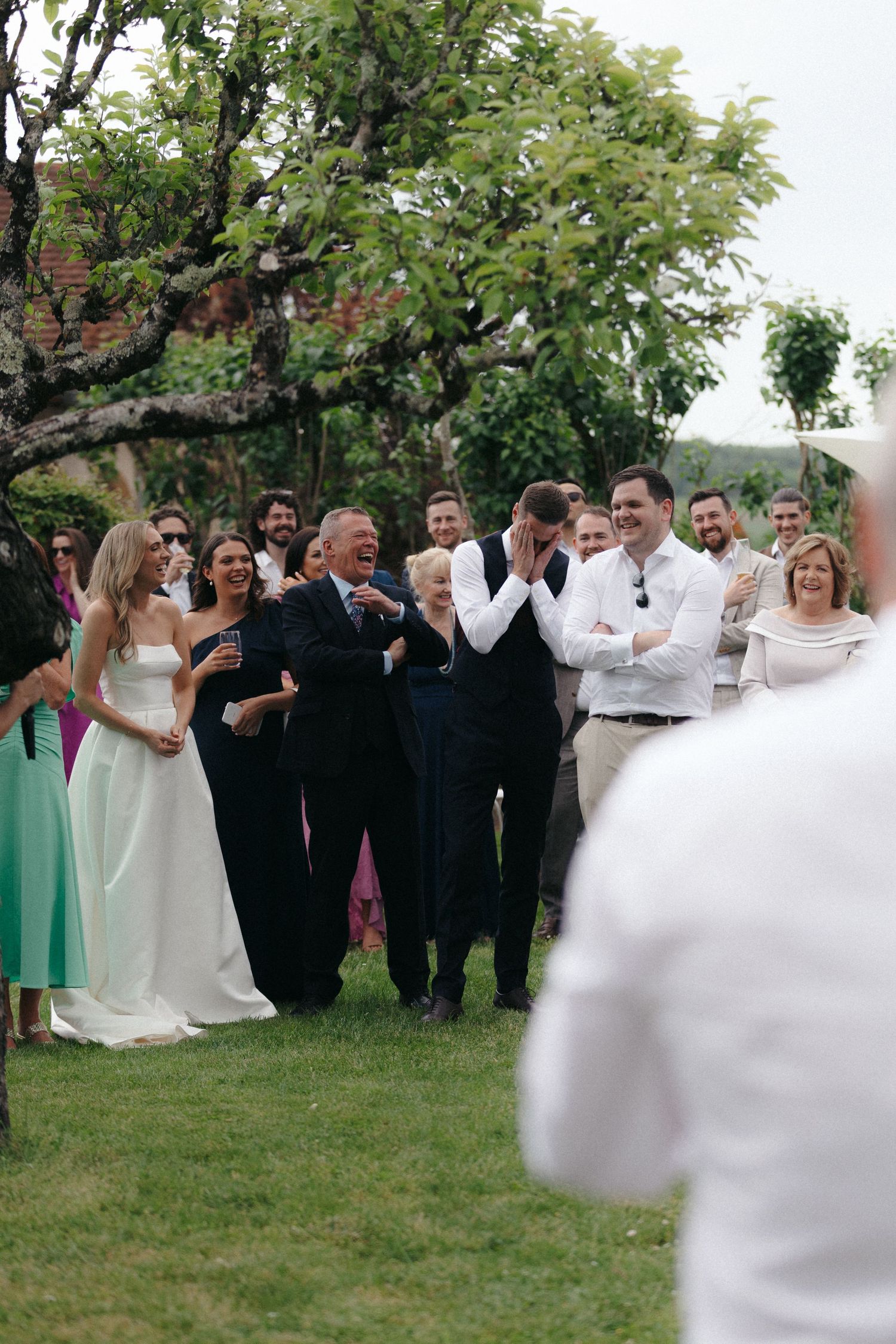 Wedding guests gather under a tree during an outdoor celebration.