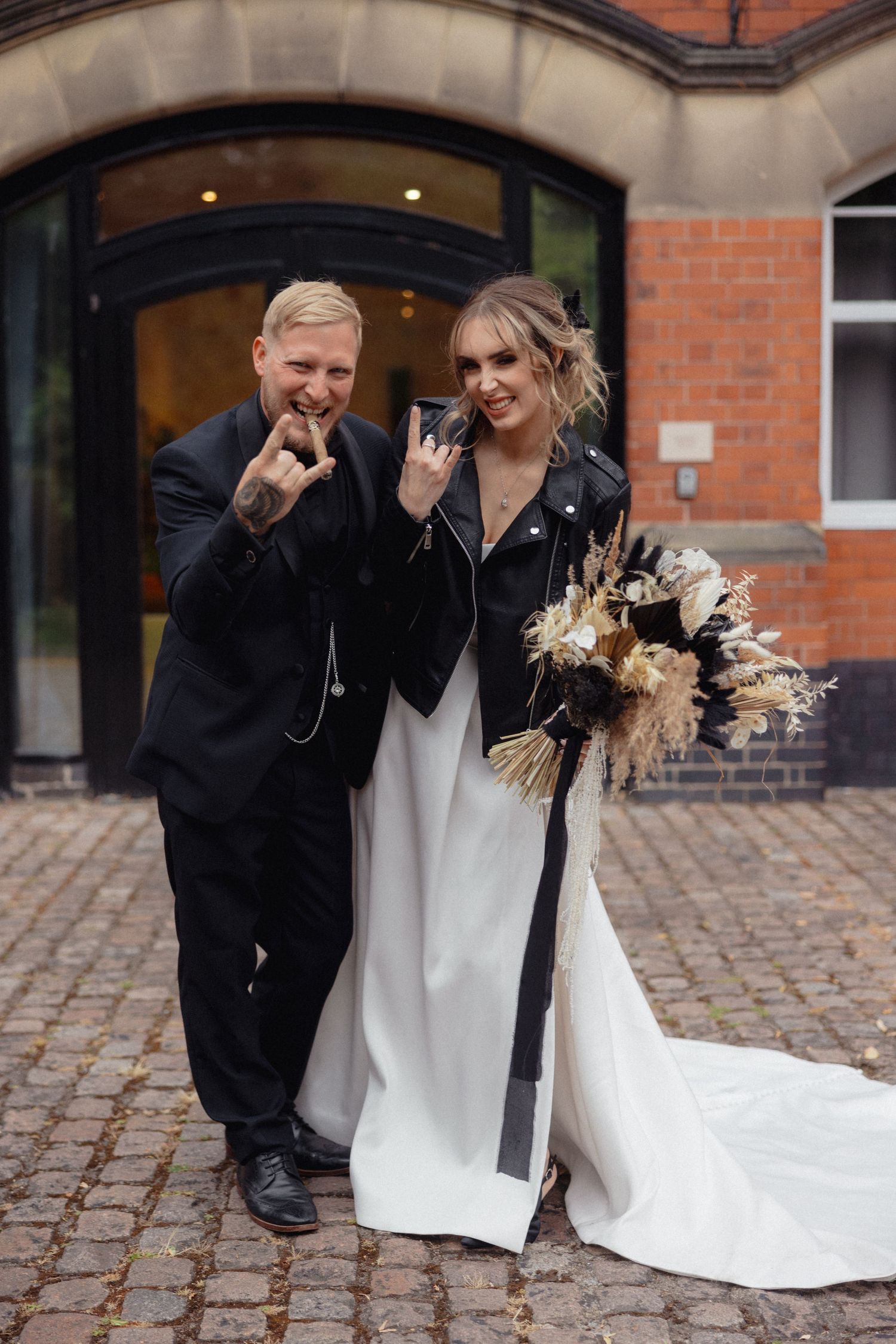 A wedding couple laughs together on cobblestone streets outside a brick building.