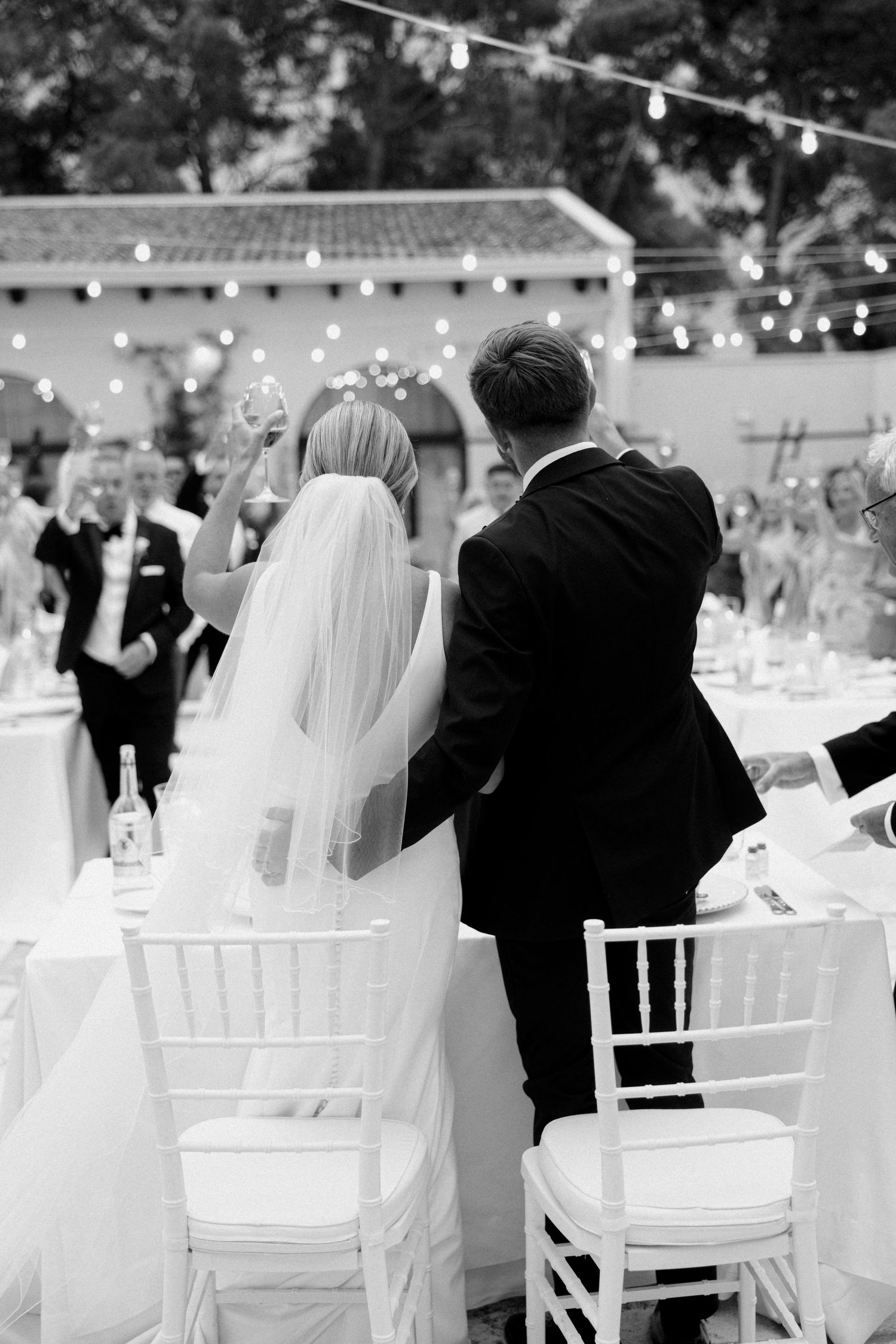Outdoor wedding reception setup with white chairs and string lights creating a romantic atmosphere.