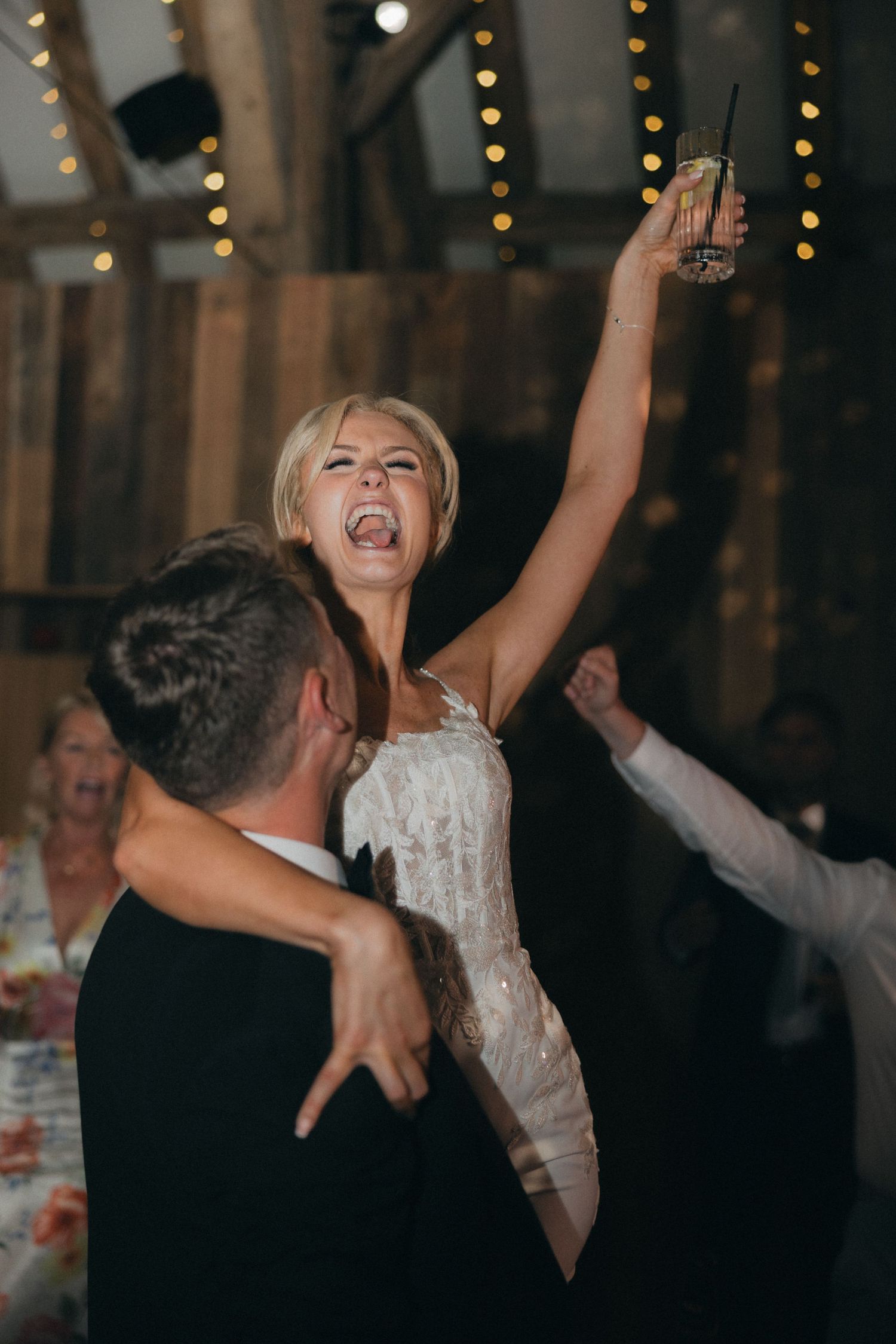 A bride laughs with joy while dancing at her wedding reception under string lights.