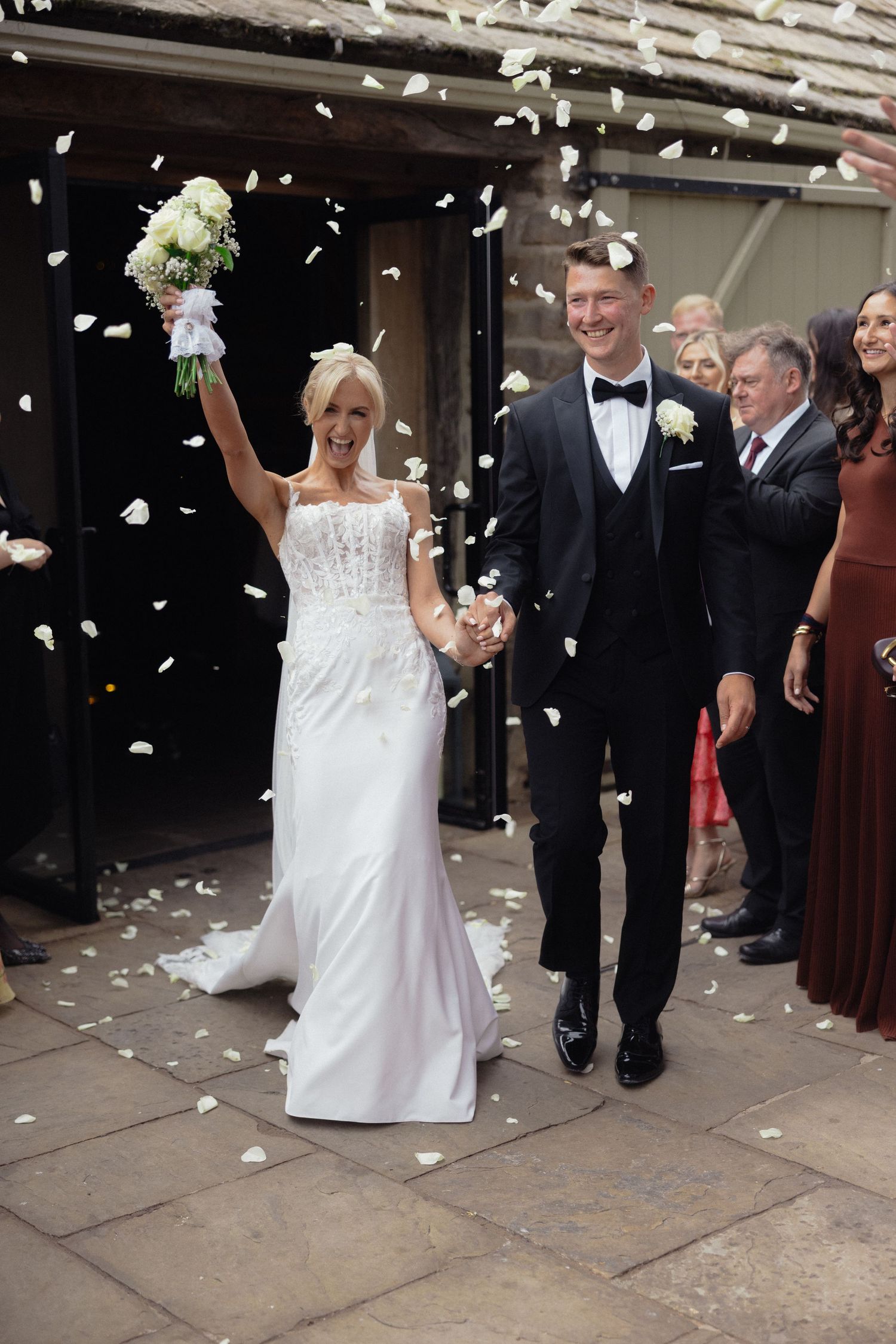 Wedding exit celebration with white flower petals being tossed by guests outside venue.