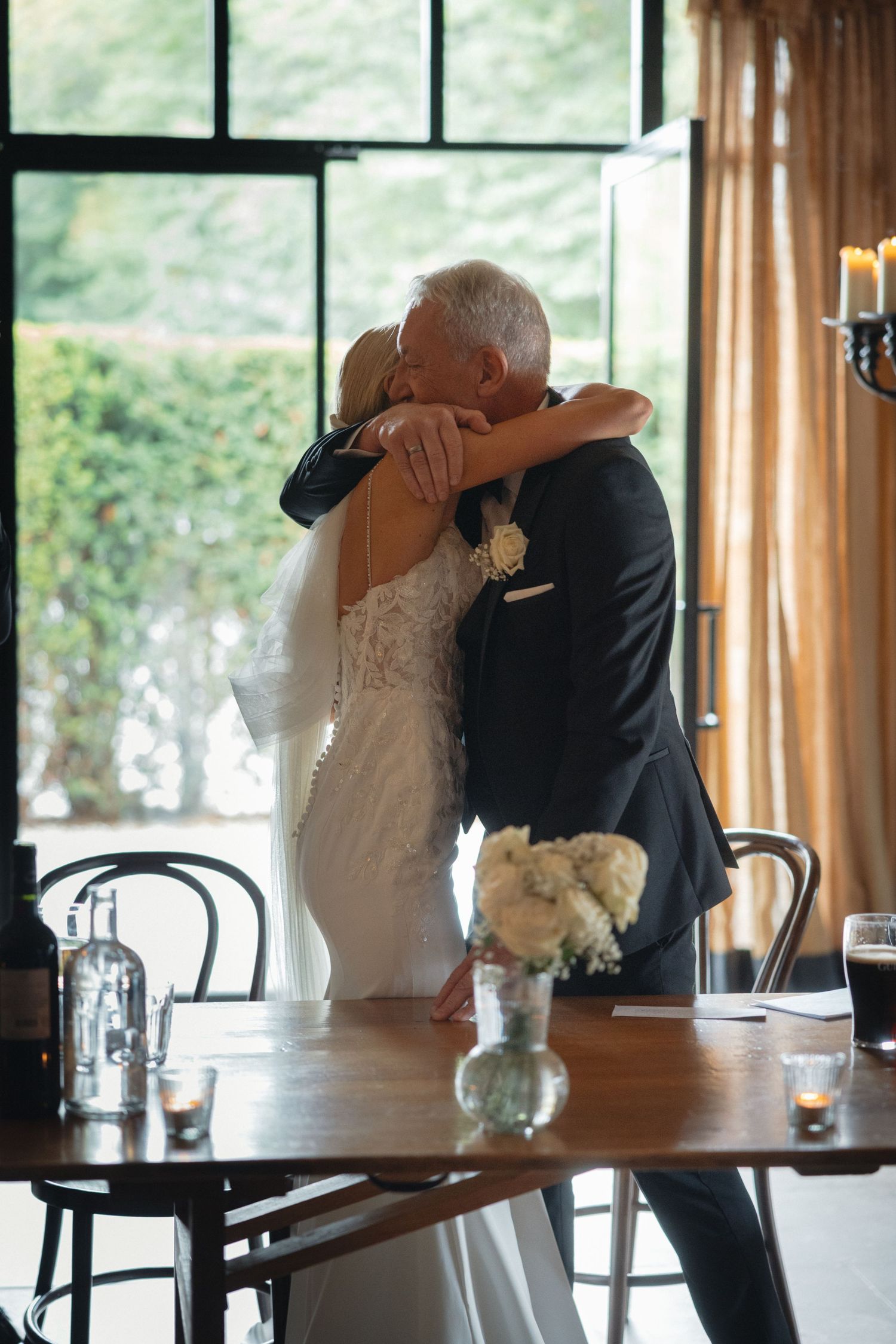 Emotional wedding moment captured at a reception with natural window lighting.