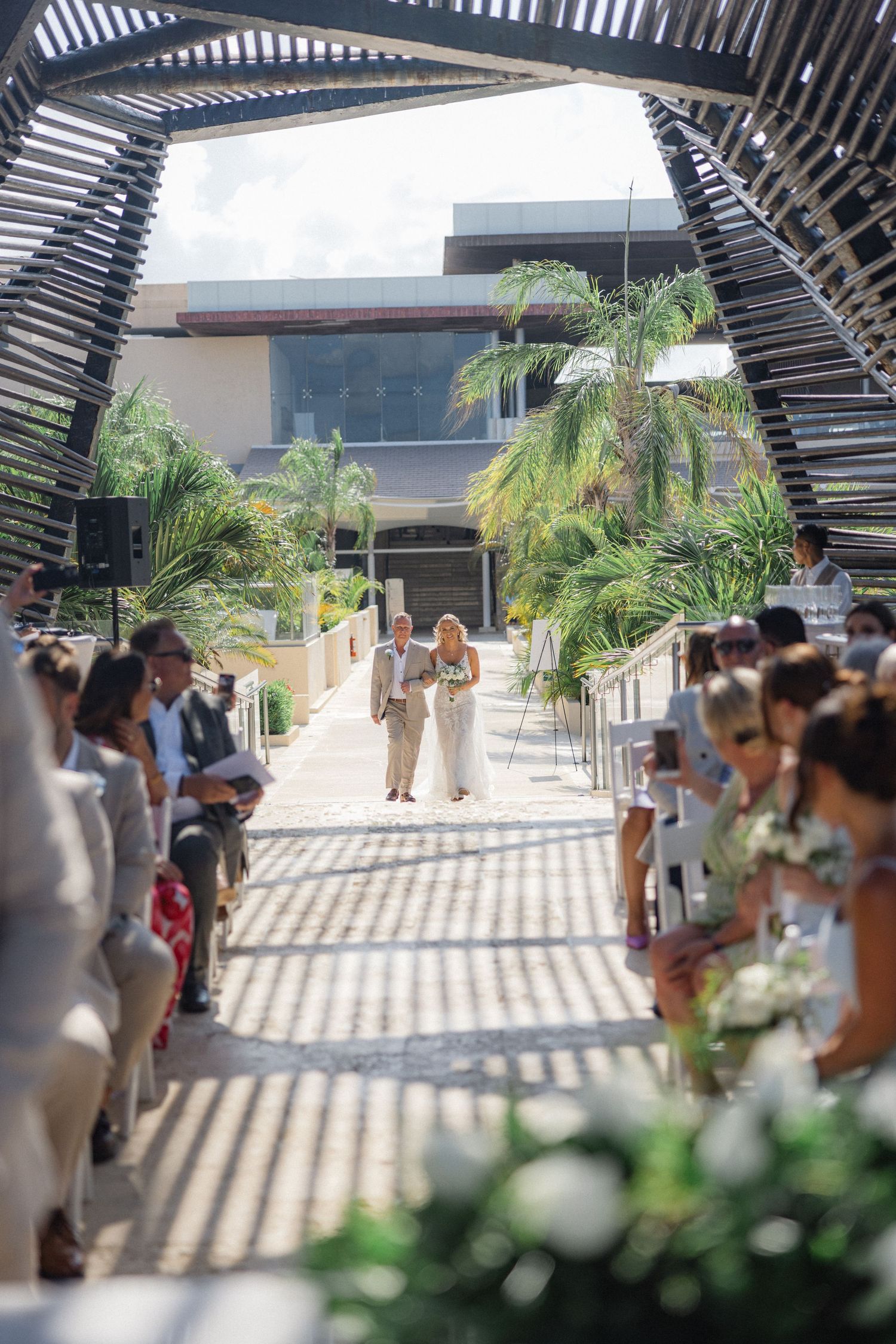 Modern outdoor wedding venue with palm trees and geometric shadows from overhead structure.