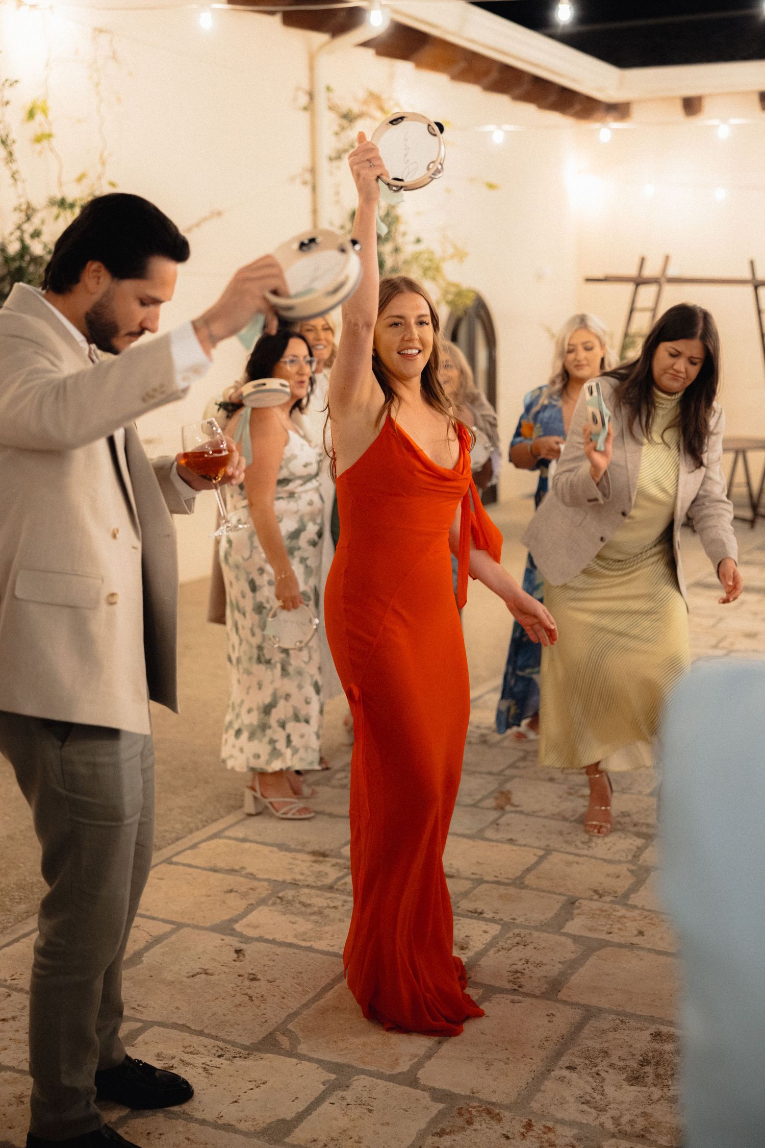 Wedding guests dance and celebrate on a stone patio with string lights overhead.
