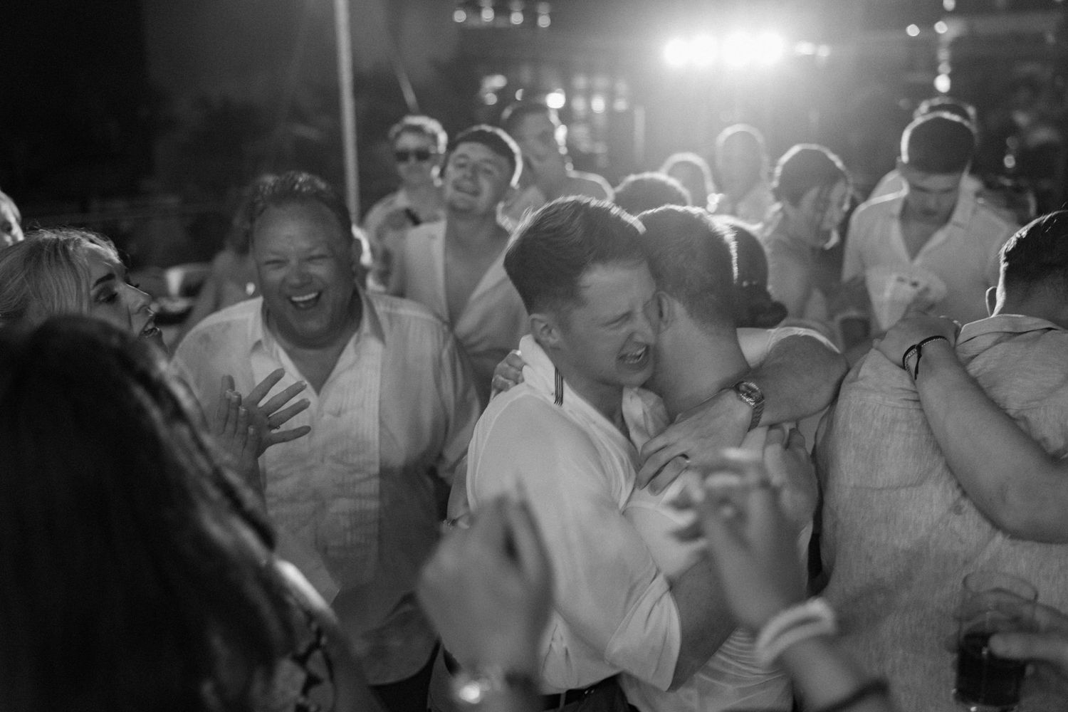 Wedding guests embrace and celebrate during an emotional moment on the dance floor.