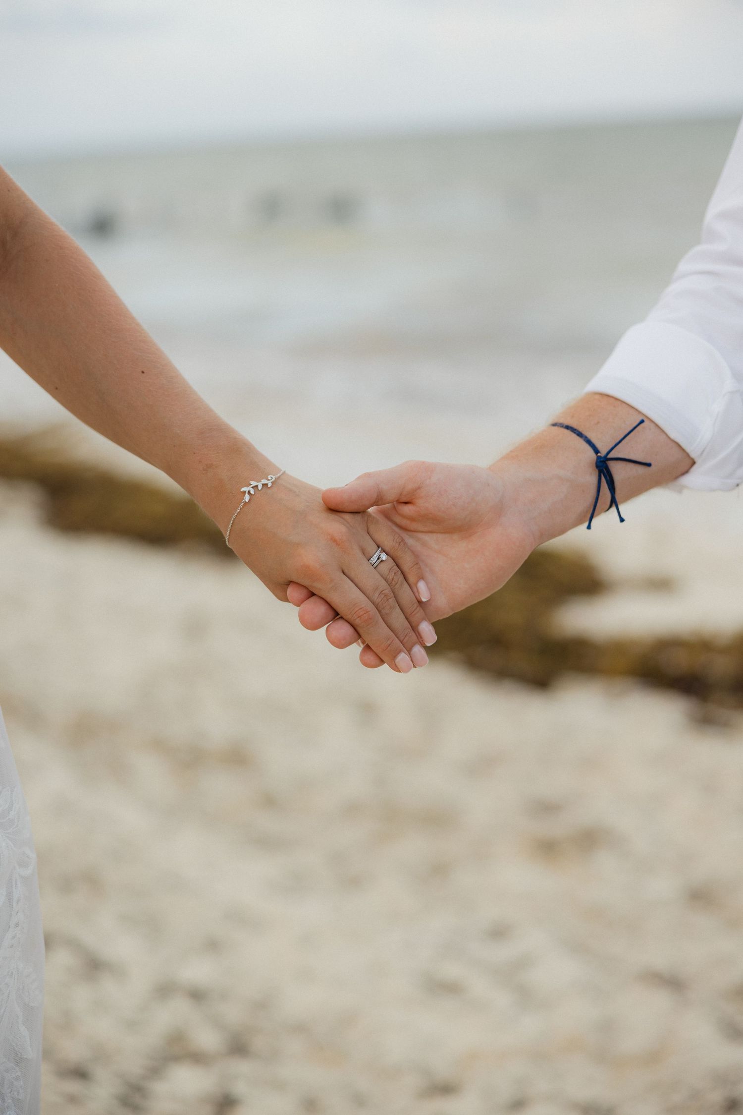 Close-up of newlyweds holding hands on beach showing wedding rings and intimate connection.