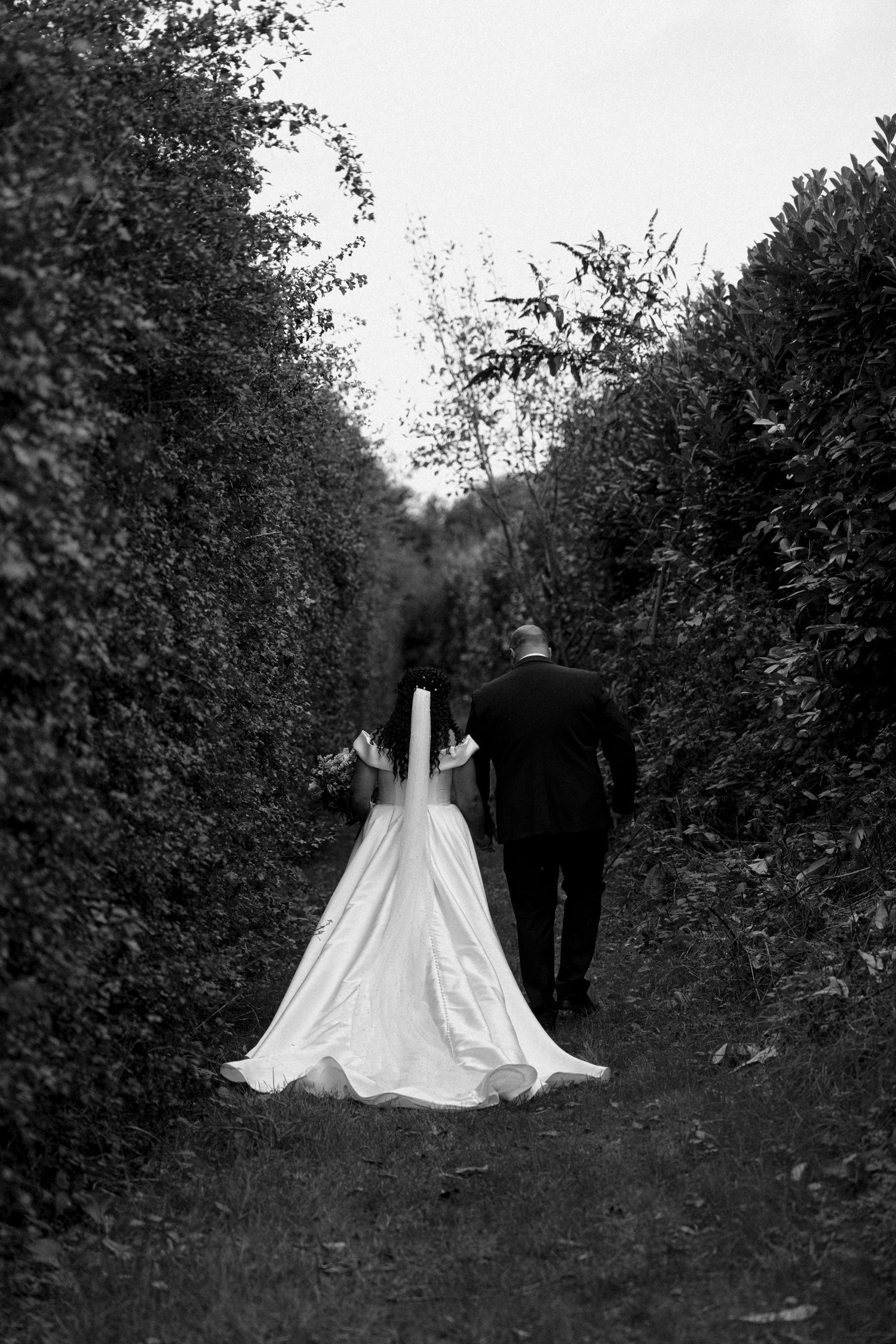 A black and white sequence of a couple walking through a tree-lined path on their wedding day.