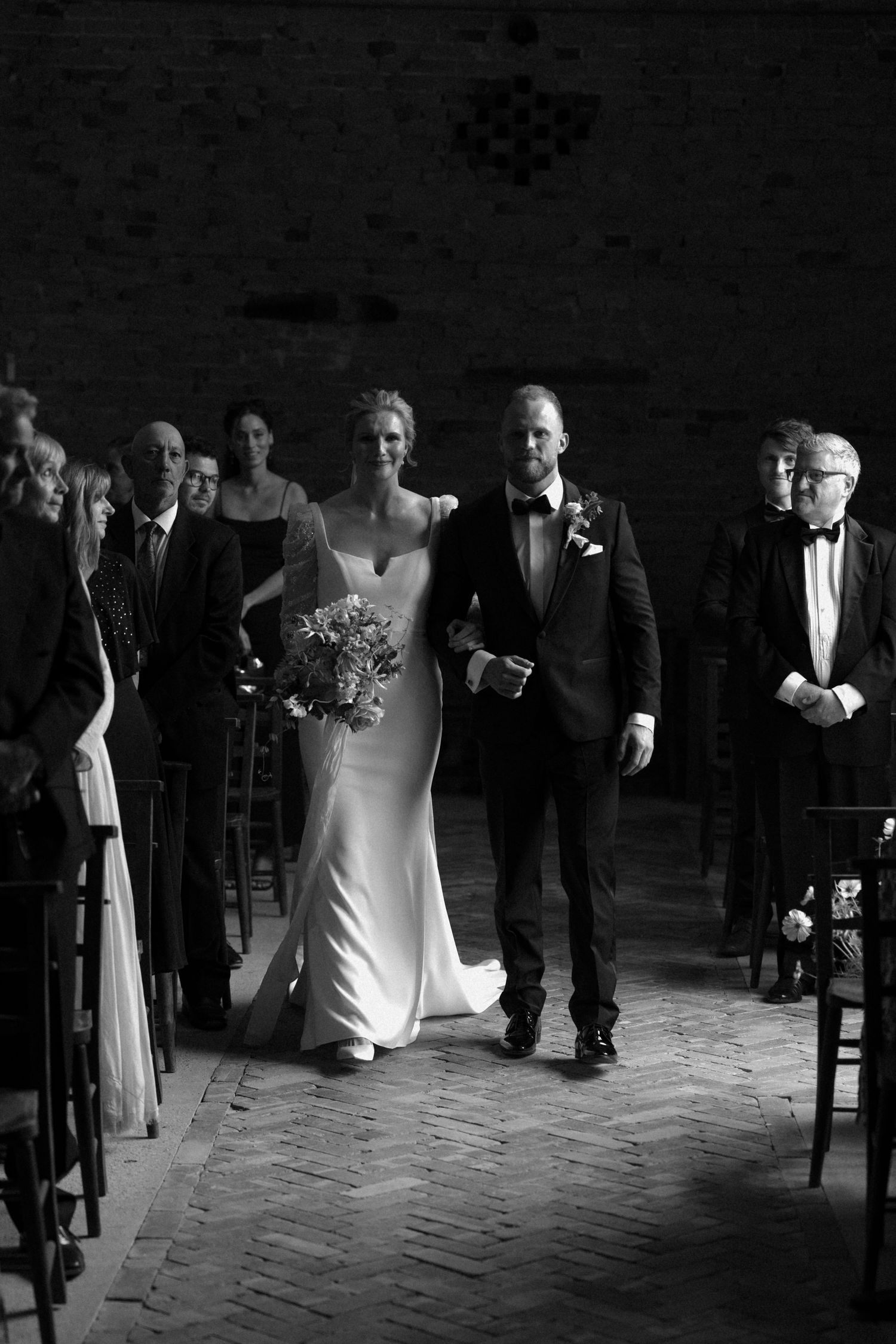 Black and white photo of wedding guests walking through an elegant indoor venue.