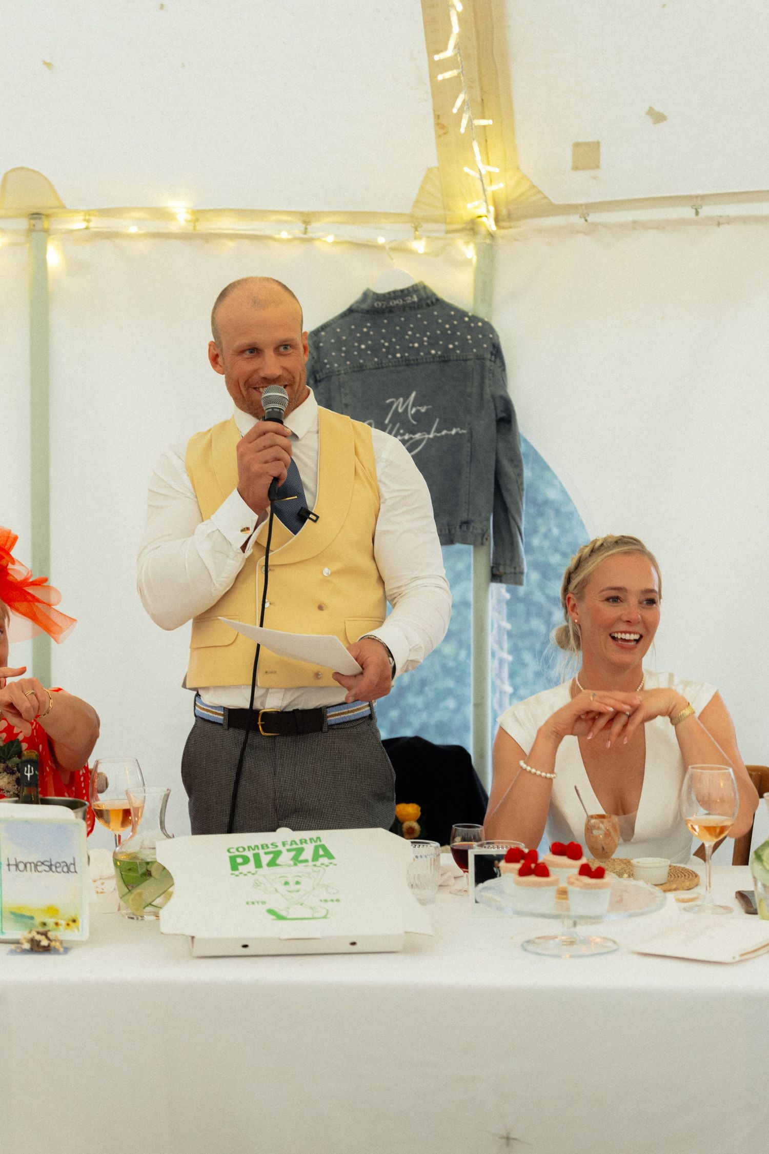 Wedding party members in formal attire share laughter during dinner at a white-decorated reception.