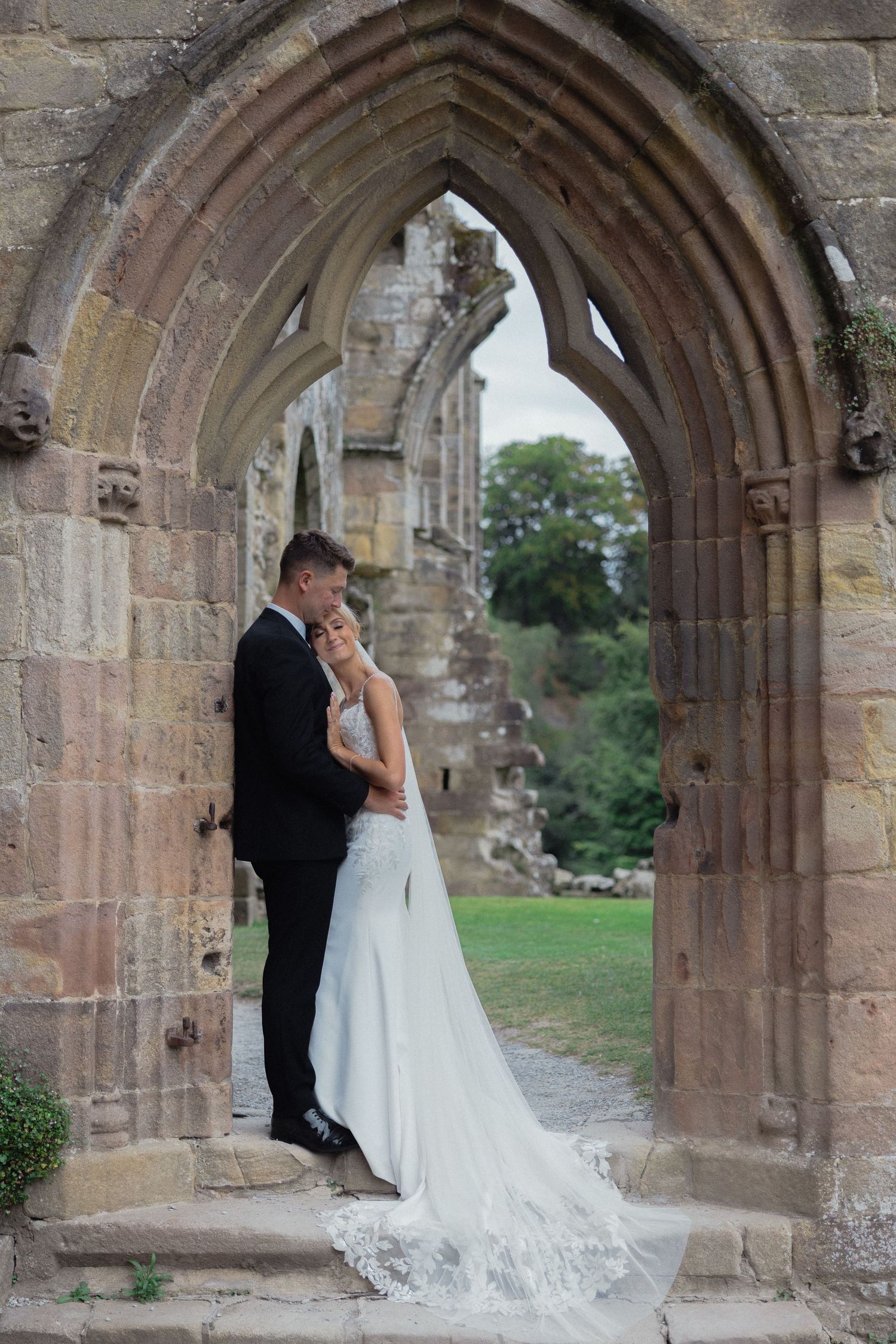 Wedding couple poses beneath gothic stone archways during romantic photoshoot.